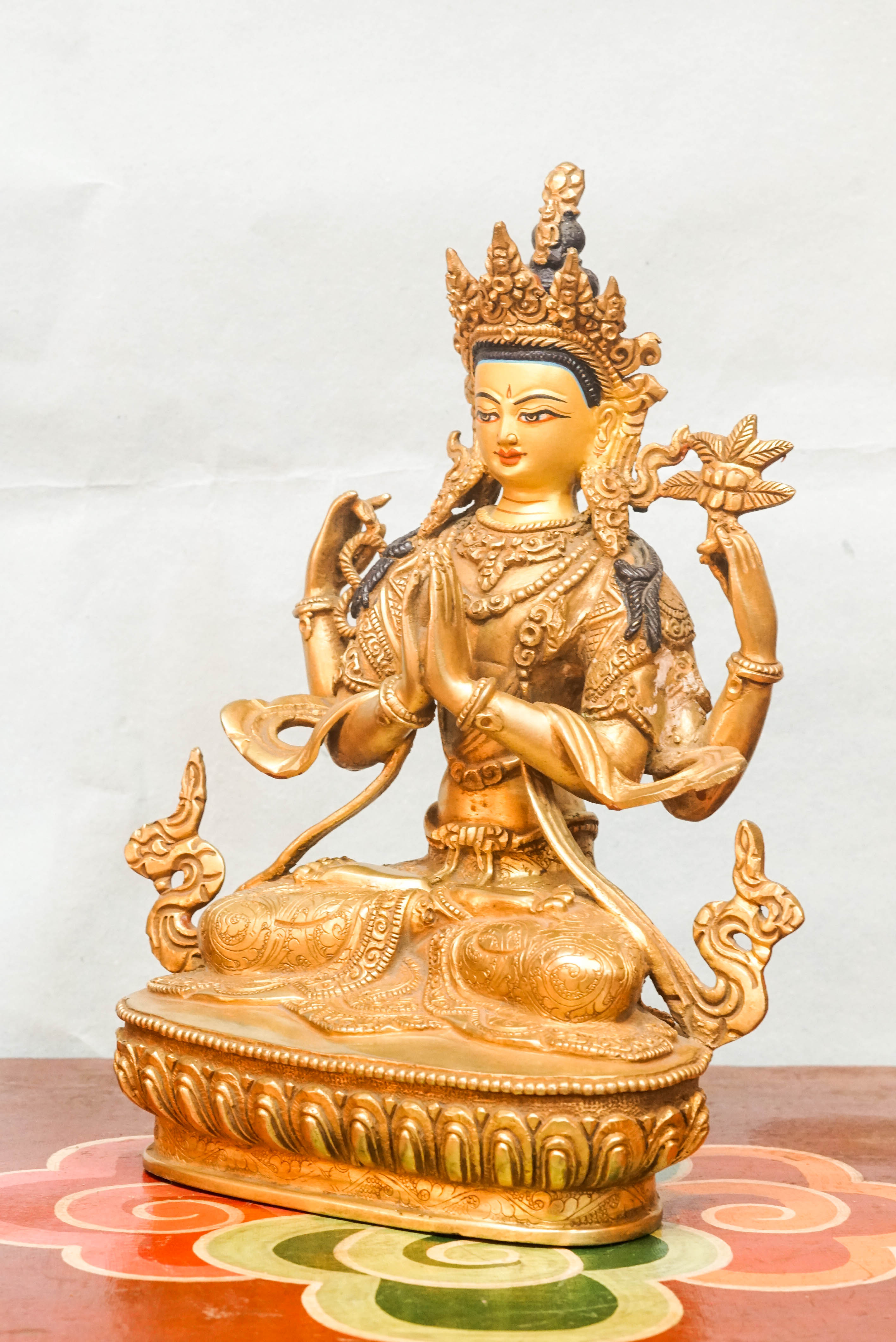 A detailed depiction of Chenrezig, seated in meditation, with multiple arms, holding a lotus flower and prayer beads, representing his vow to relieve the suffering of all beings.