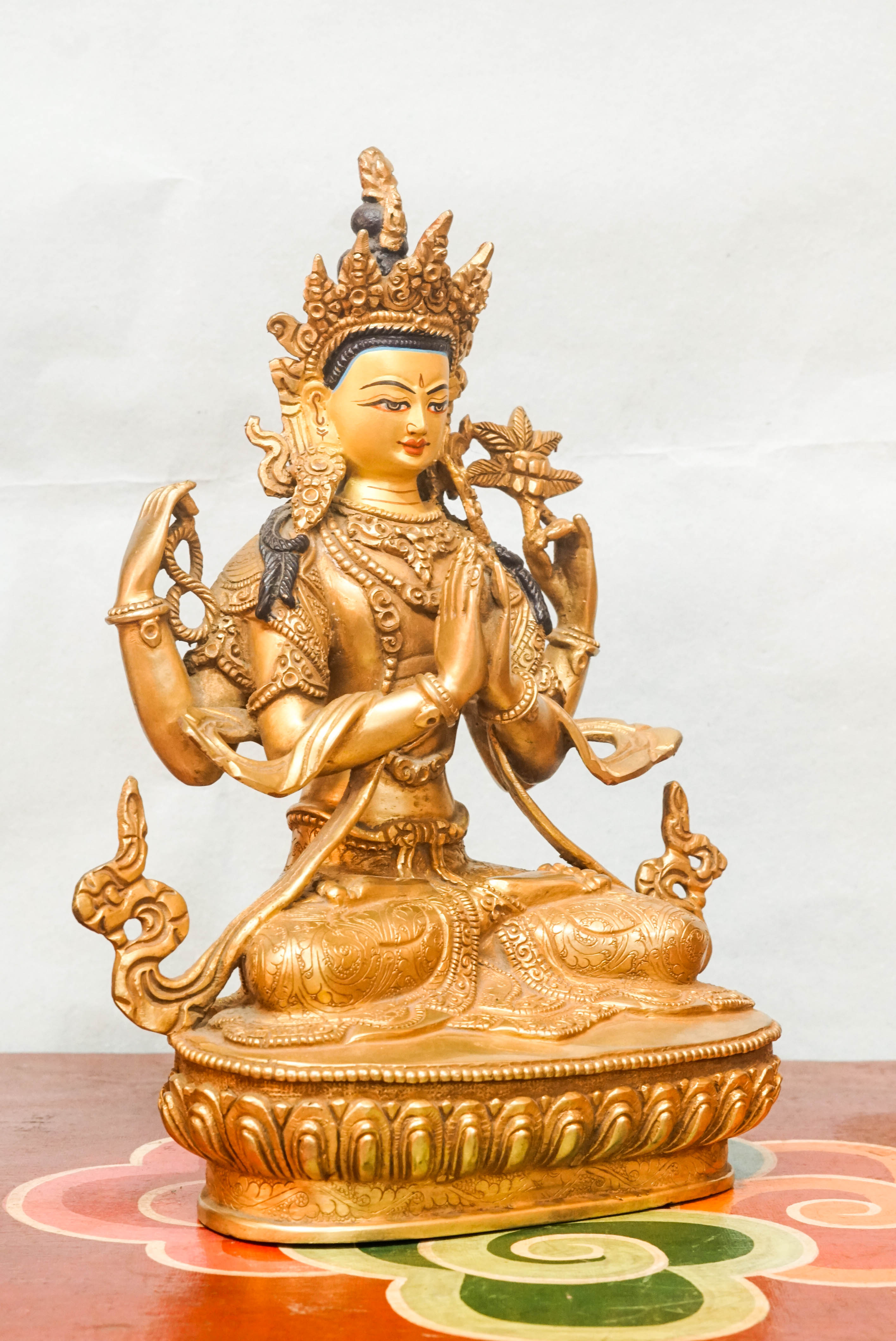 A detailed depiction of Chenrezig, seated in meditation, with multiple arms, holding a lotus flower and prayer beads, representing his vow to relieve the suffering of all beings.