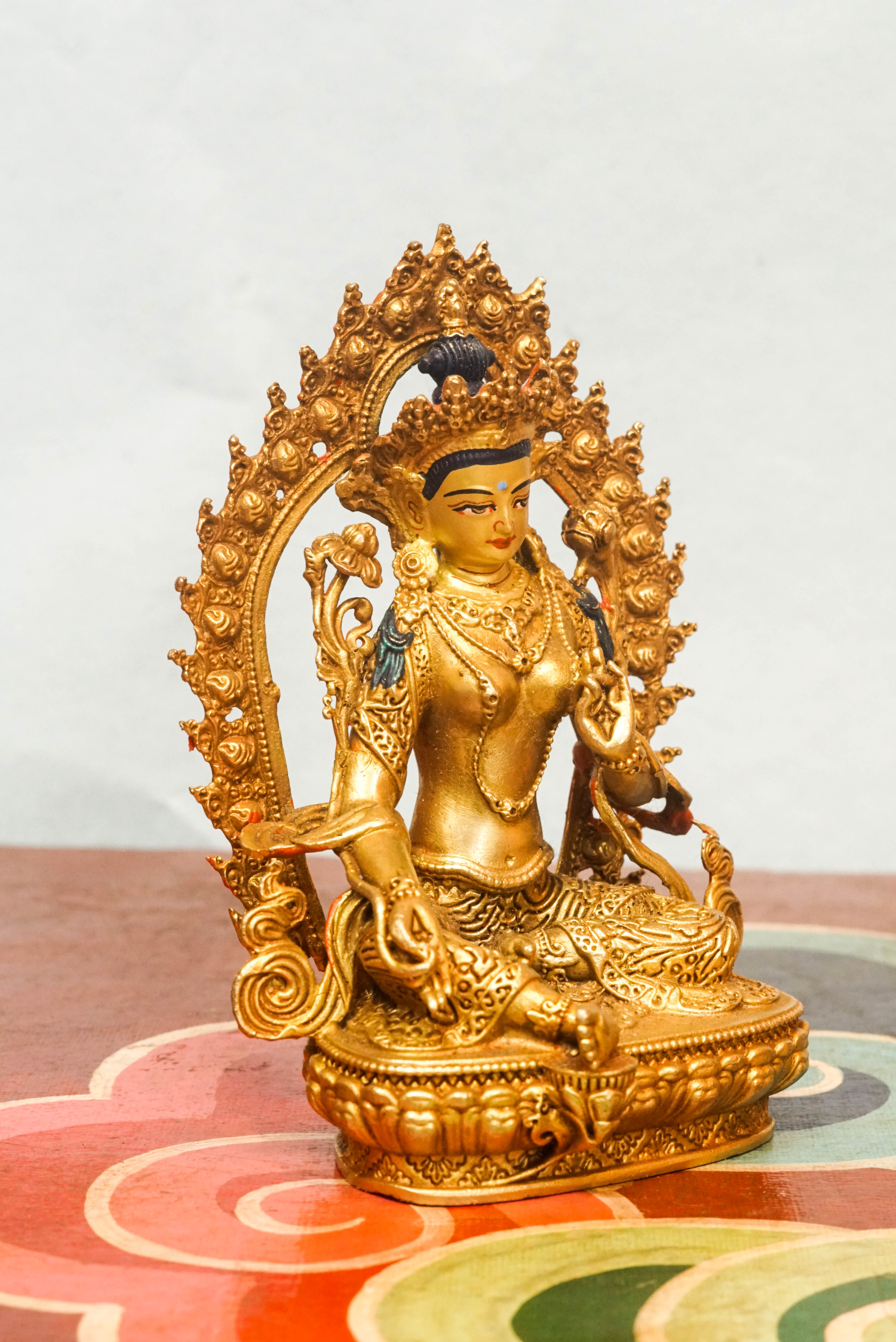Gold-plated statue of Green Tara, set in a decorative frame, representing the Bodhisattva of compassion and swift action.