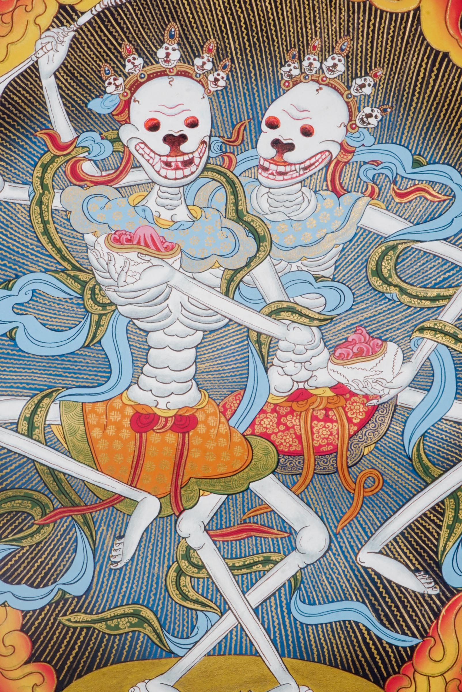 Traditional Tibetan thangka painting depicting the Skeleton Dance (Chitipati), showing two crowned skeleton figures dancing together within a ring of flames, surrounded by clouds and a symbolic landscape.