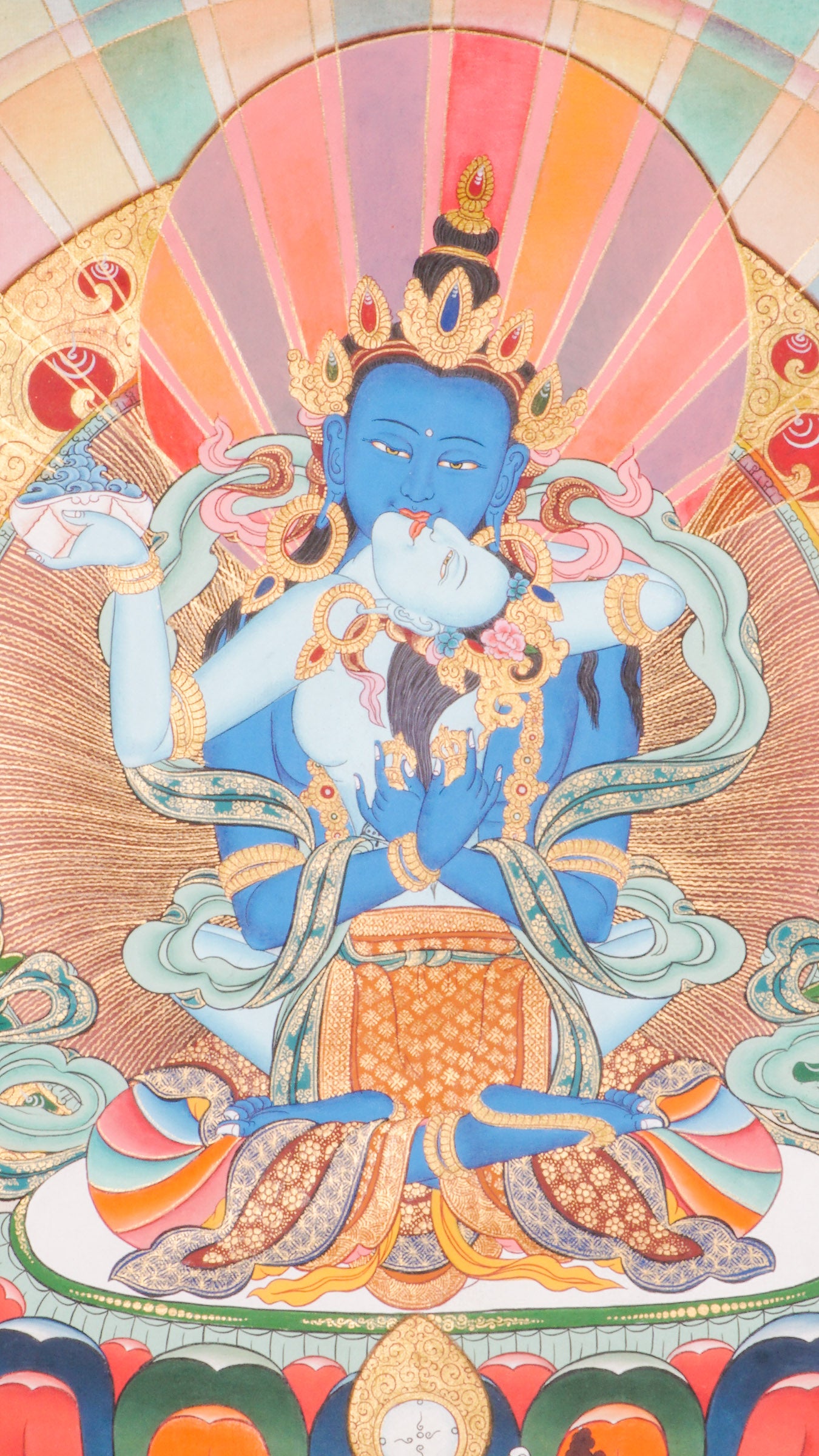 Traditional Tibetan thangka painting depicting Vajradhara Shakti in union, shown as a blue deity seated on a lotus throne with a consort, surrounded by radiant rays, clouds, floral motifs, and a symbolic landscape.
