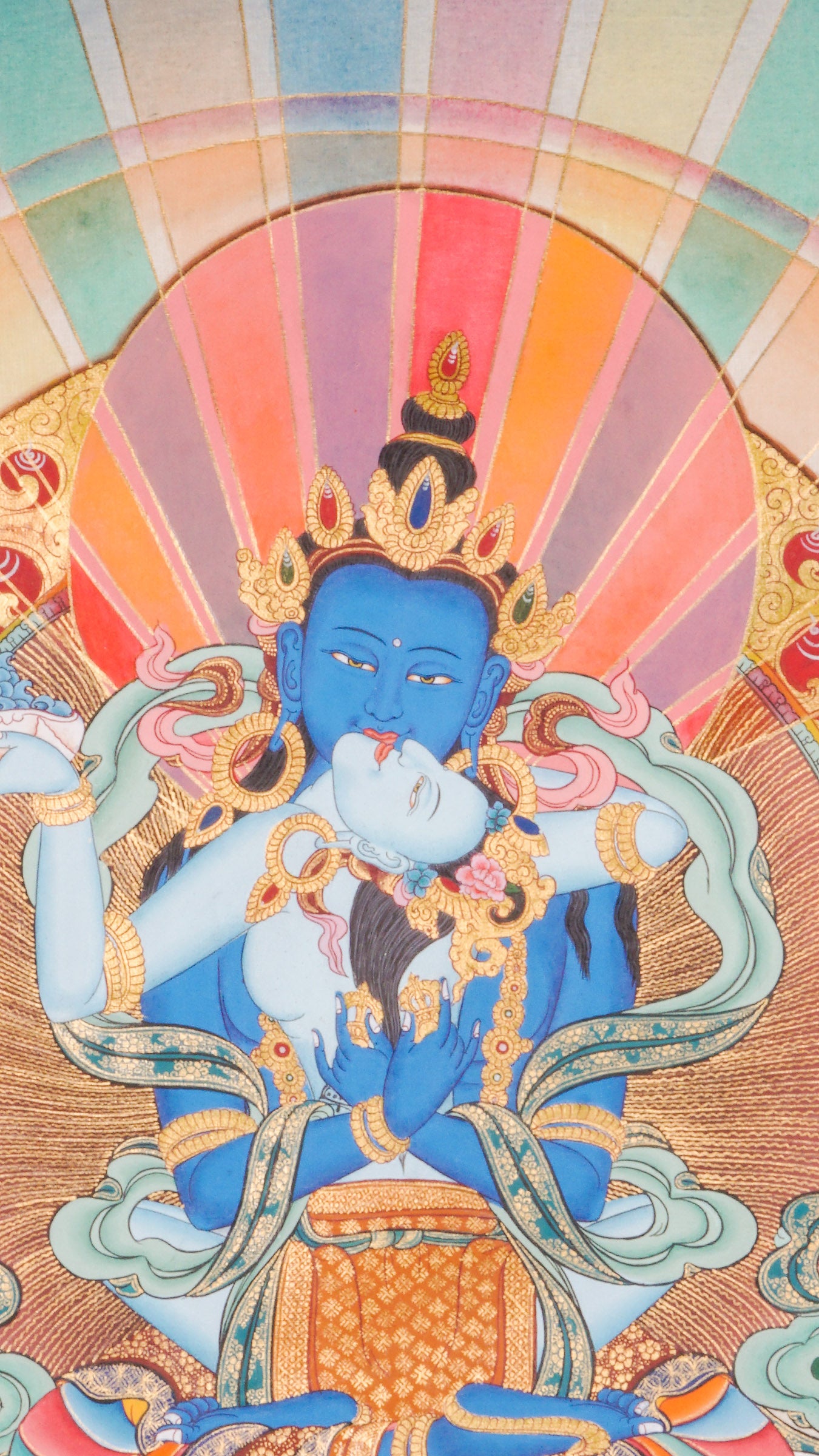 Traditional Tibetan thangka painting depicting Vajradhara Shakti in union, shown as a blue deity seated on a lotus throne with a consort, surrounded by radiant rays, clouds, floral motifs, and a symbolic landscape.