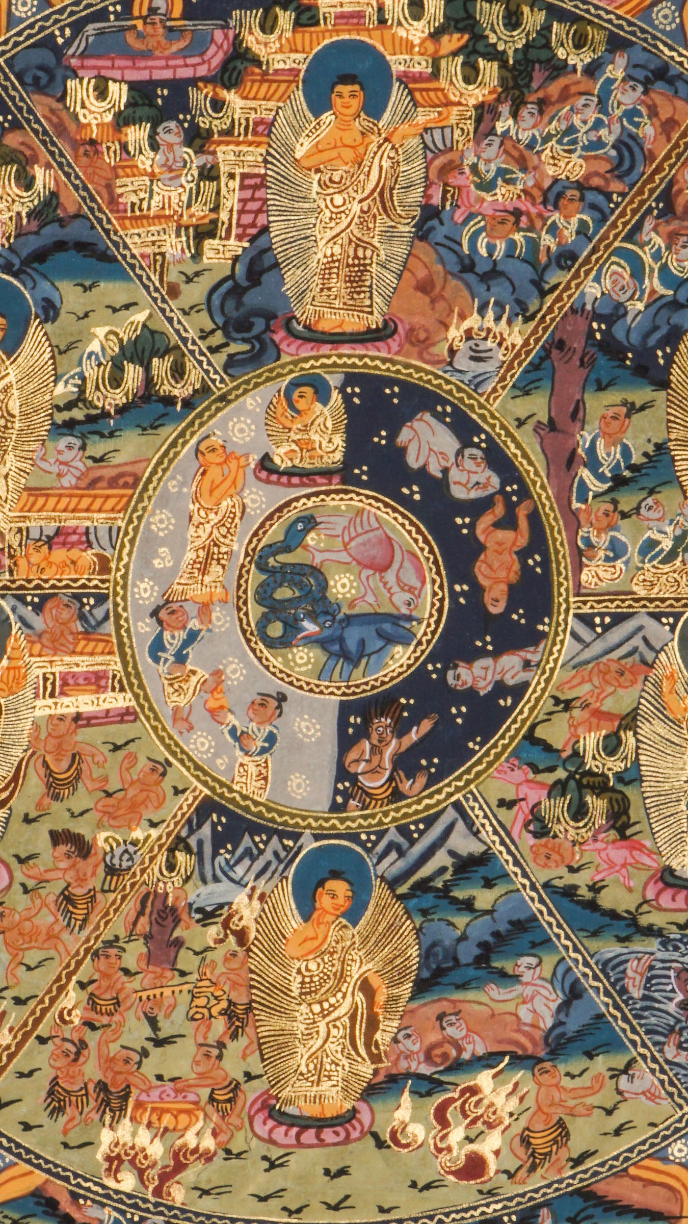 Detailed thangka-style painting showing a large circular wheel divided into multiple sections filled with small human figures, animals, buildings, and landscape scenes, surrounded by concentric decorative rings and held by a large blue multi-eyed figure with extended arms, set against a dark background with clouds, flames, and ornate gold, red, and blue patterns.