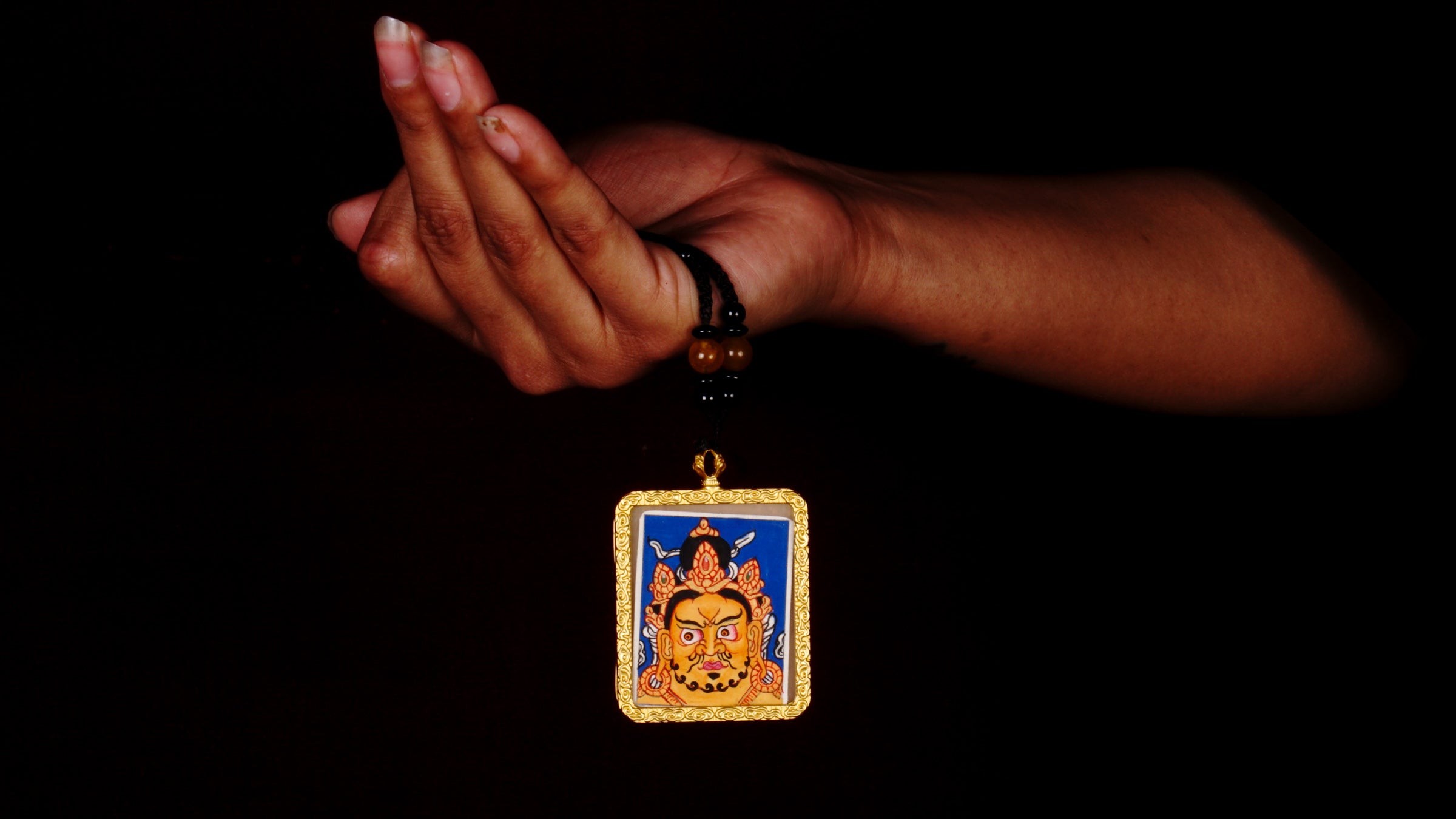 Hand-painted Zambala wealth deity miniature Thangka pendant in gold-accented copper Ghau locket with black beaded cord.