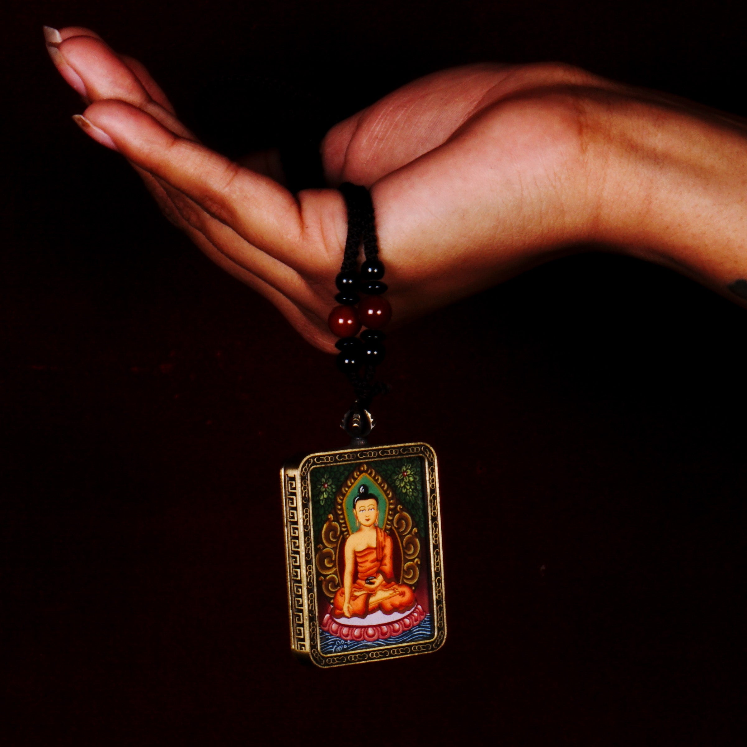 Hand-painted Shakyamuni Buddha miniature Thangka pendant in gold-accented copper Ghau locket with black beaded cord.