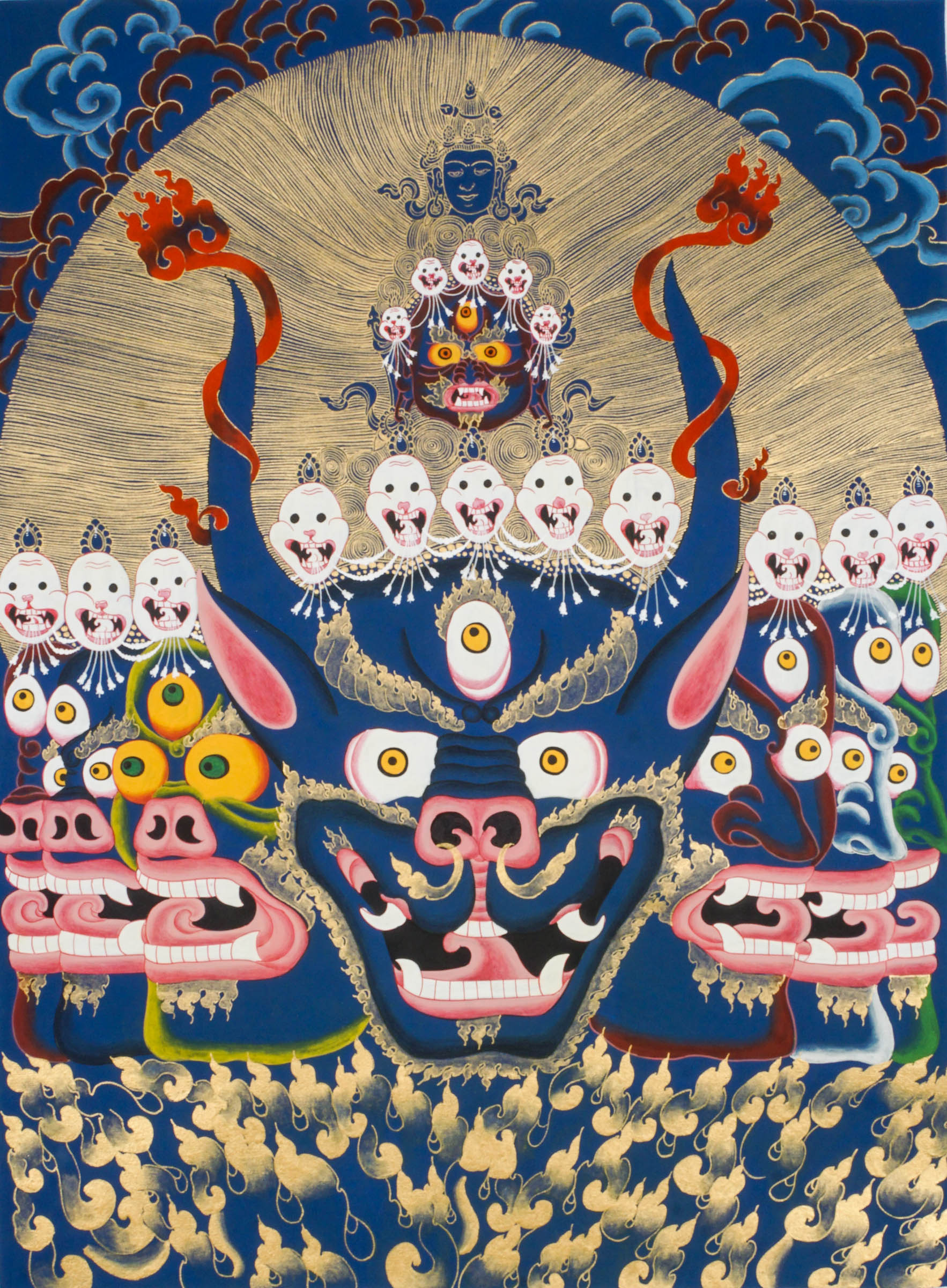 Thangka painting showing a large blue multi-faced figure with numerous eyes and open mouths, crowned by smaller faces and skull motifs, set against a gold halo and stylized cloud background.