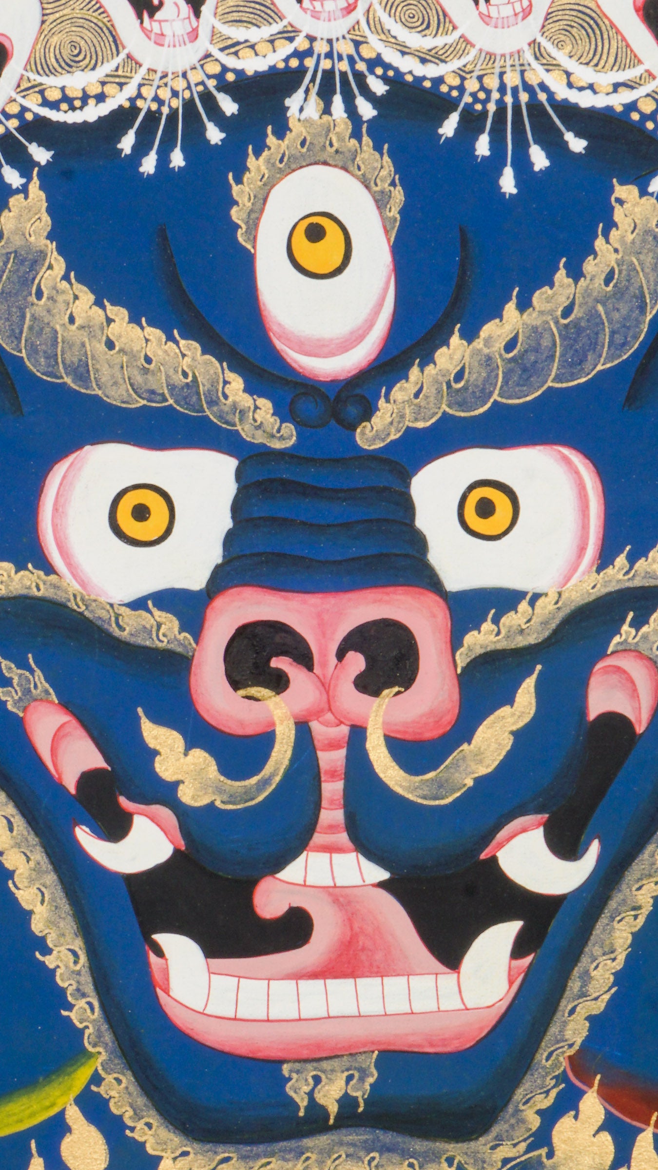 Thangka painting showing a large blue multi-faced figure with numerous eyes and open mouths, crowned by smaller faces and skull motifs, set against a gold halo and stylized cloud background.