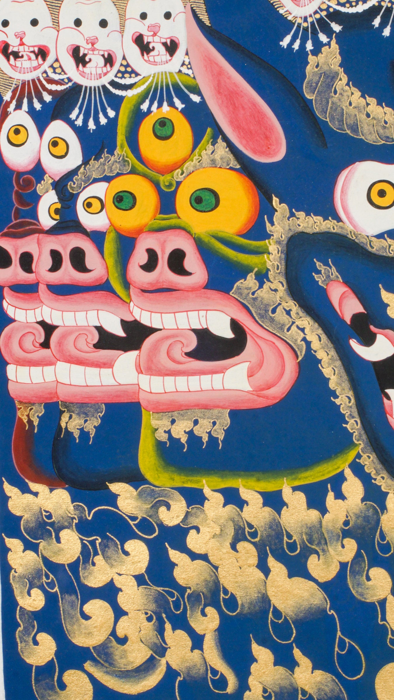 Thangka painting showing a large blue multi-faced figure with numerous eyes and open mouths, crowned by smaller faces and skull motifs, set against a gold halo and stylized cloud background.