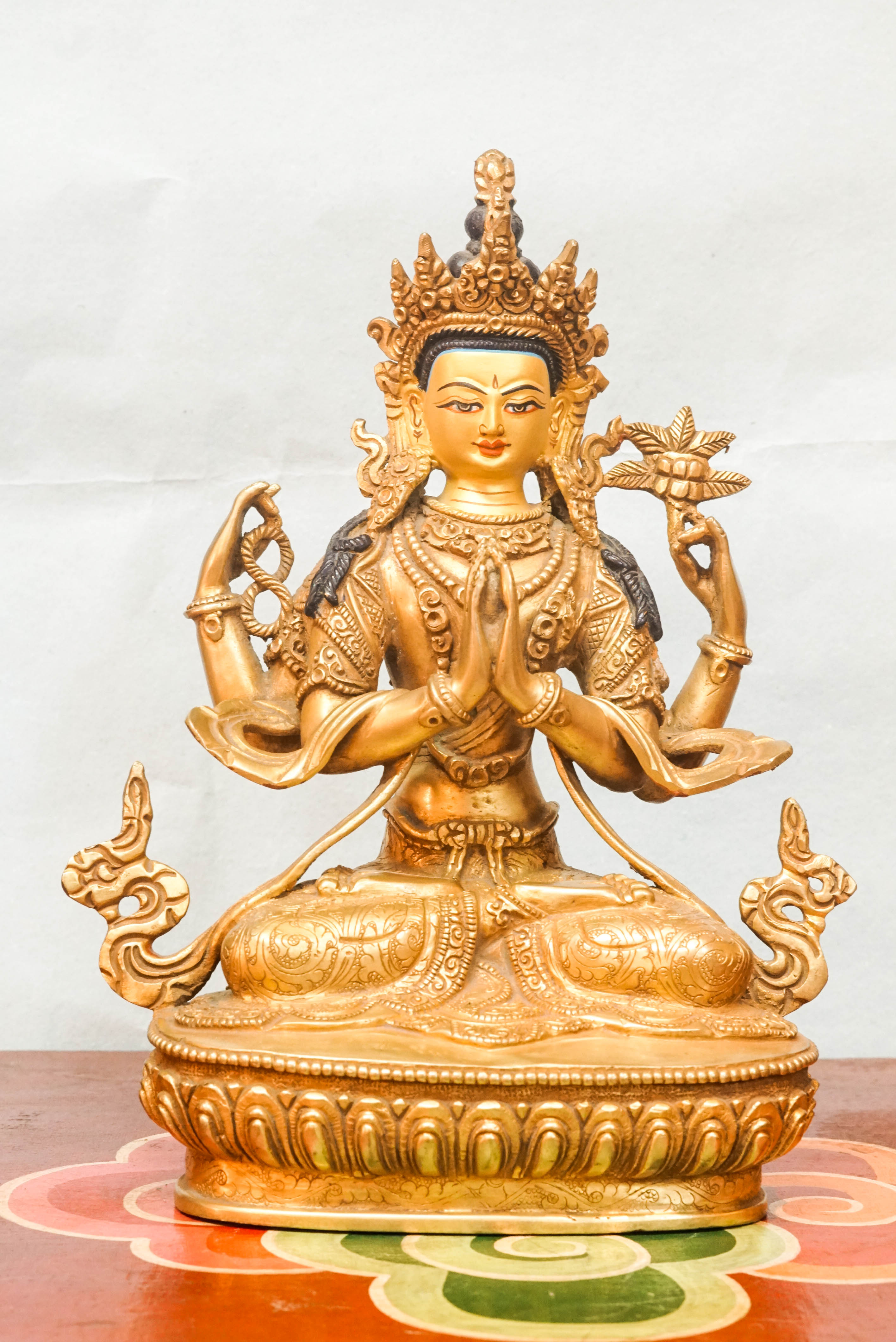 A detailed depiction of Chenrezig, seated in meditation, with multiple arms, holding a lotus flower and prayer beads, representing his vow to relieve the suffering of all beings.