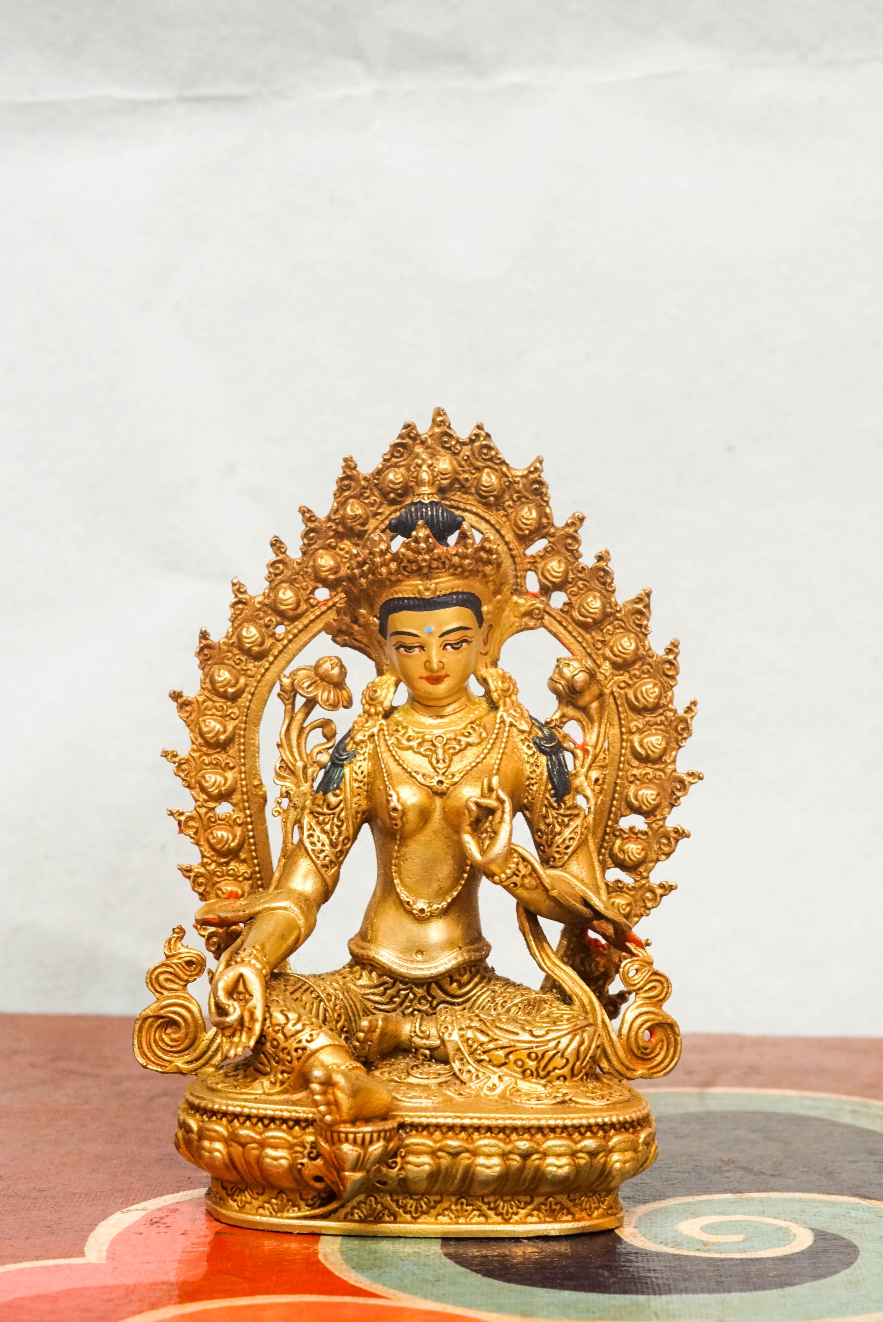 Gold-plated statue of Green Tara, set in a decorative frame, representing the Bodhisattva of compassion and swift action.