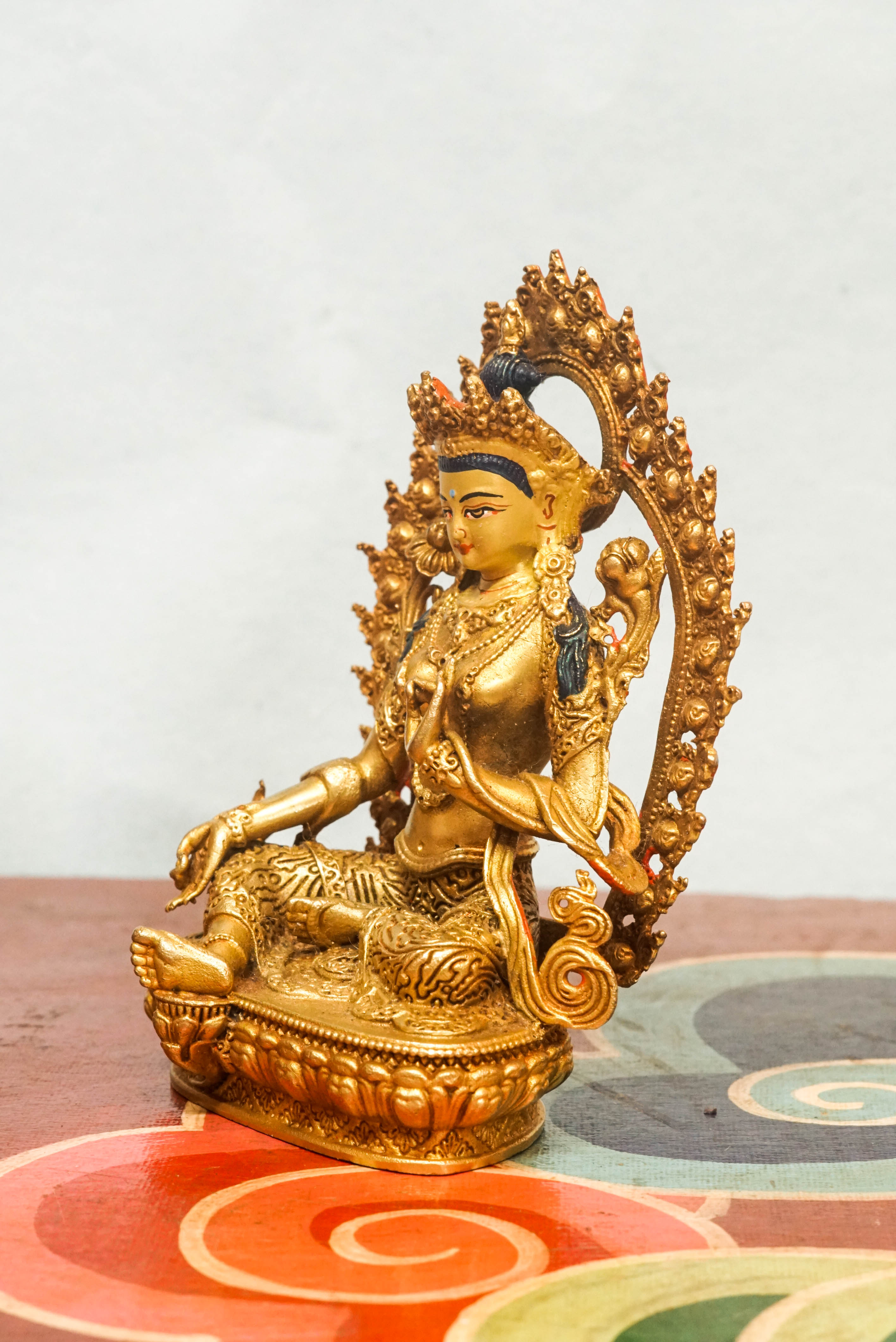 Gold-plated statue of Green Tara, set in a decorative frame, representing the Bodhisattva of compassion and swift action.