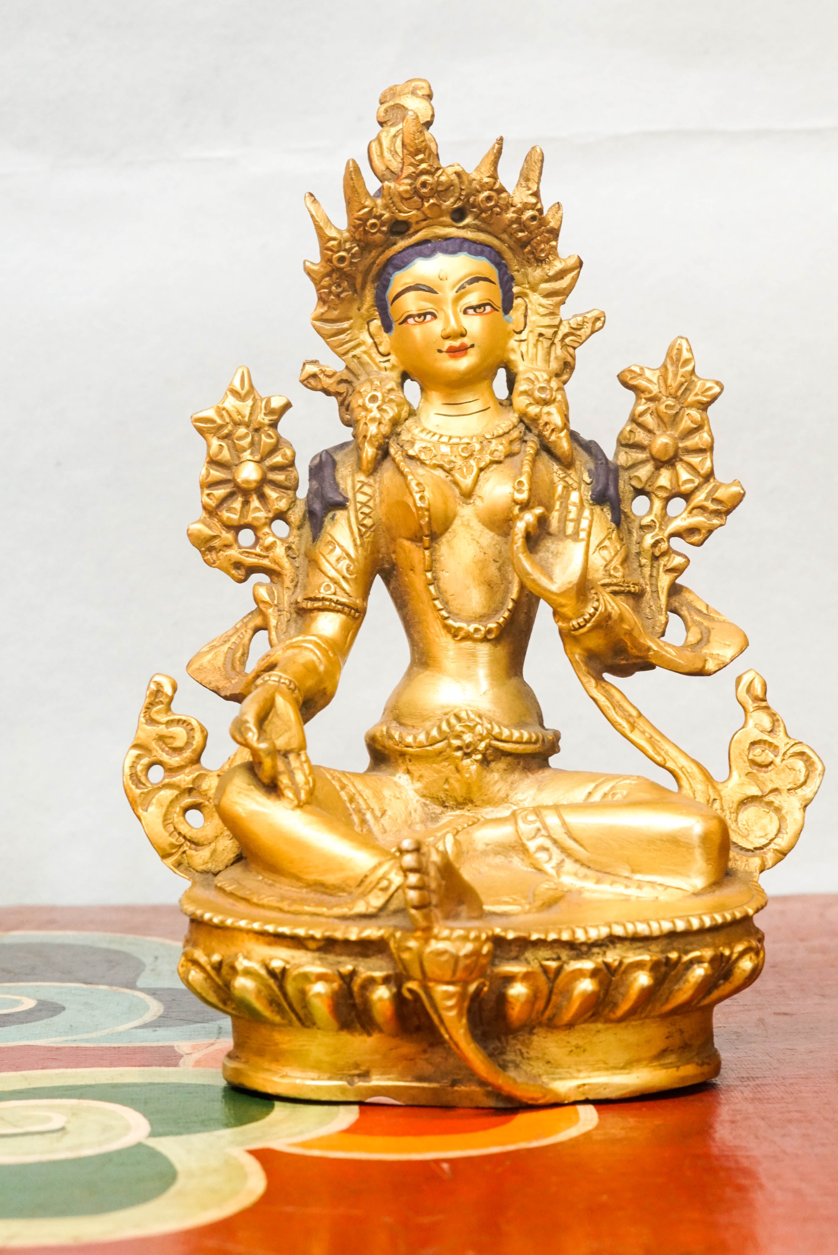 Green Tara statue seated on a lotus pedestal, with one leg extended and hands in protective and giving mudras, symbolizing her swift response to the suffering of sentient beings.