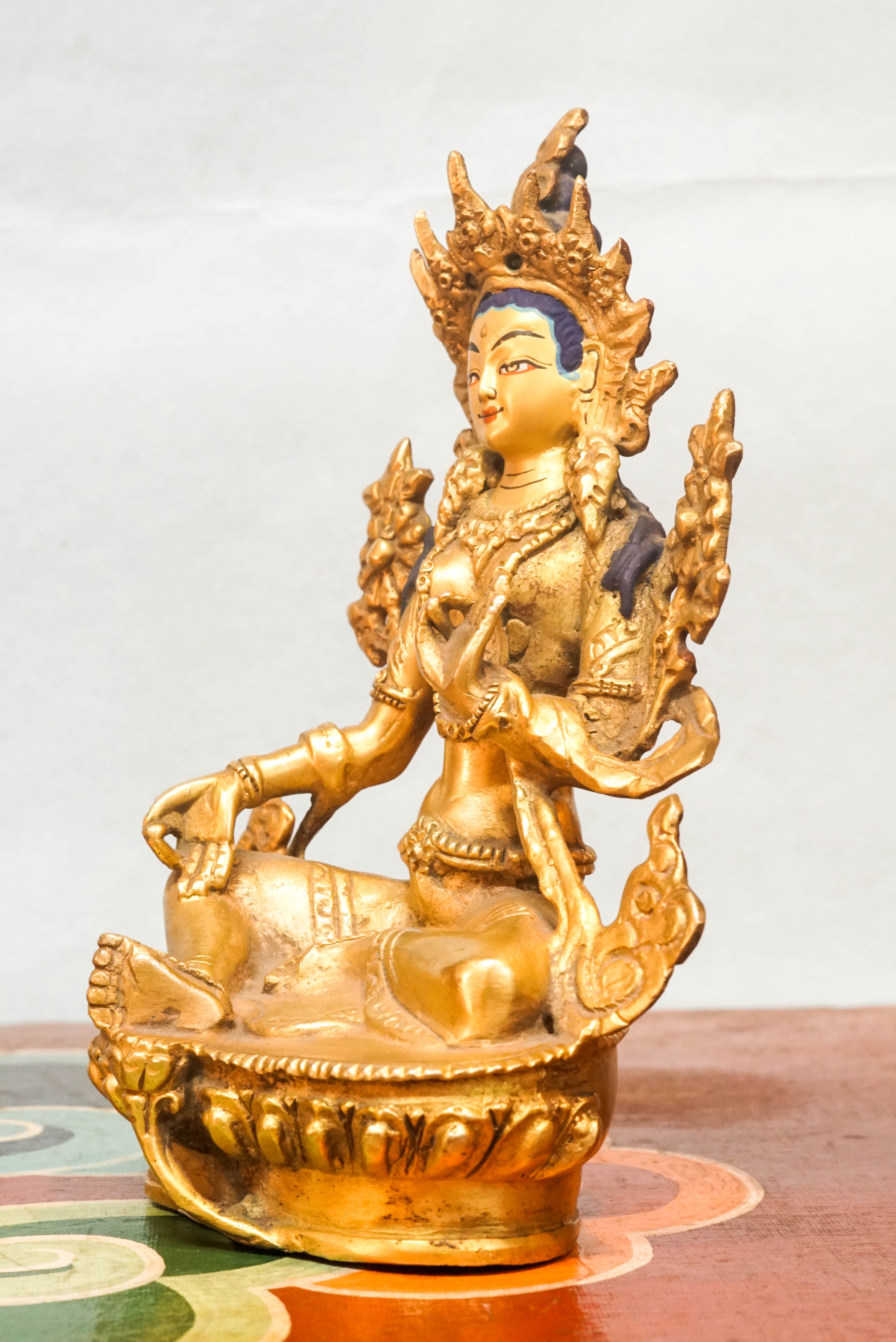 Green Tara statue seated on a lotus pedestal, with one leg extended and hands in protective and giving mudras, symbolizing her swift response to the suffering of sentient beings.