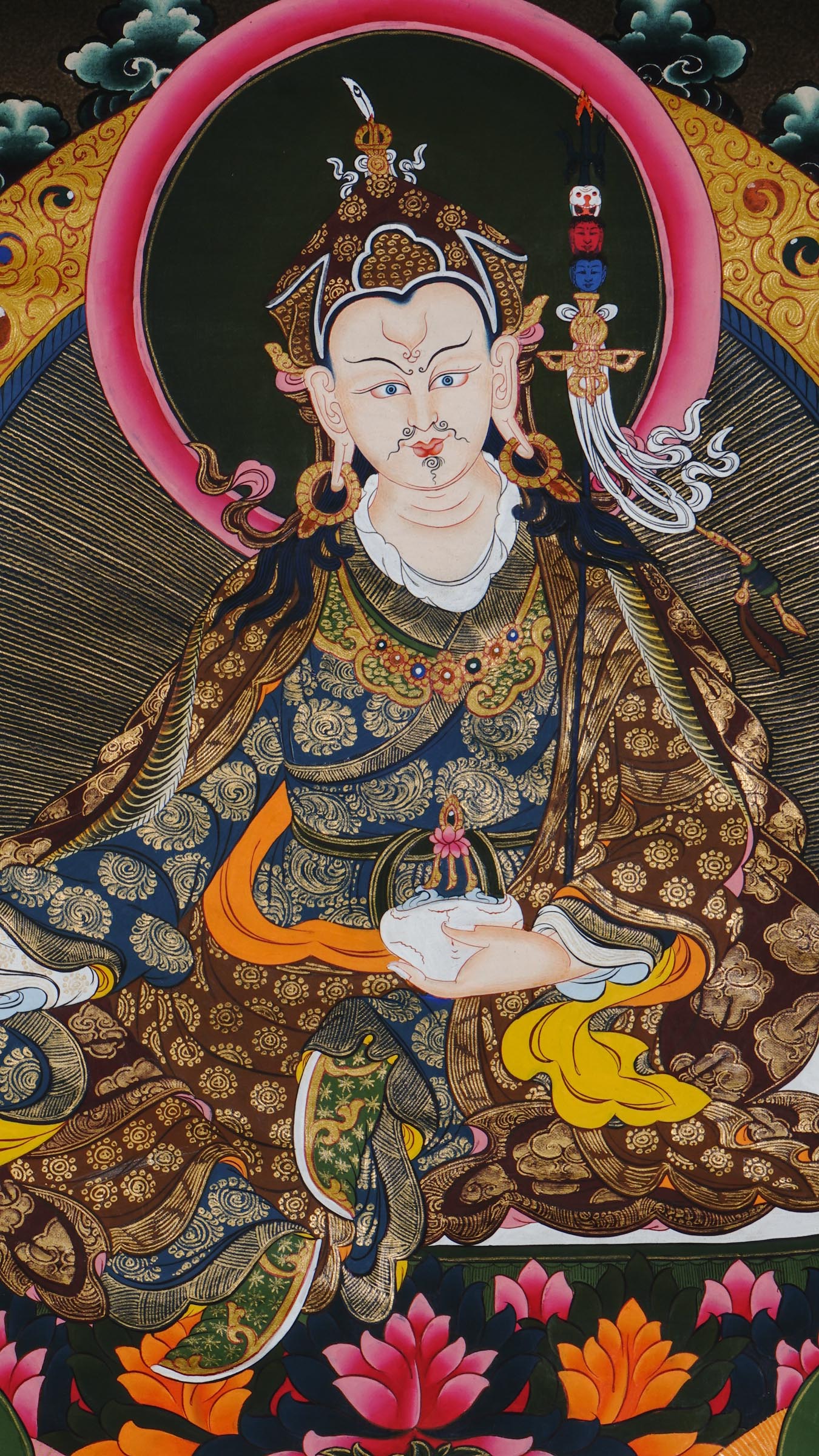 Hand-painted Guru Rinpoche thangka from Kathmandu, Nepal showing the master seated on a lotus throne holding a vajra, skull cup, and khatvanga staff with symbolic heads, adorned with robes, jewelry, and halo in traditional Tibetan Vajrayana style.