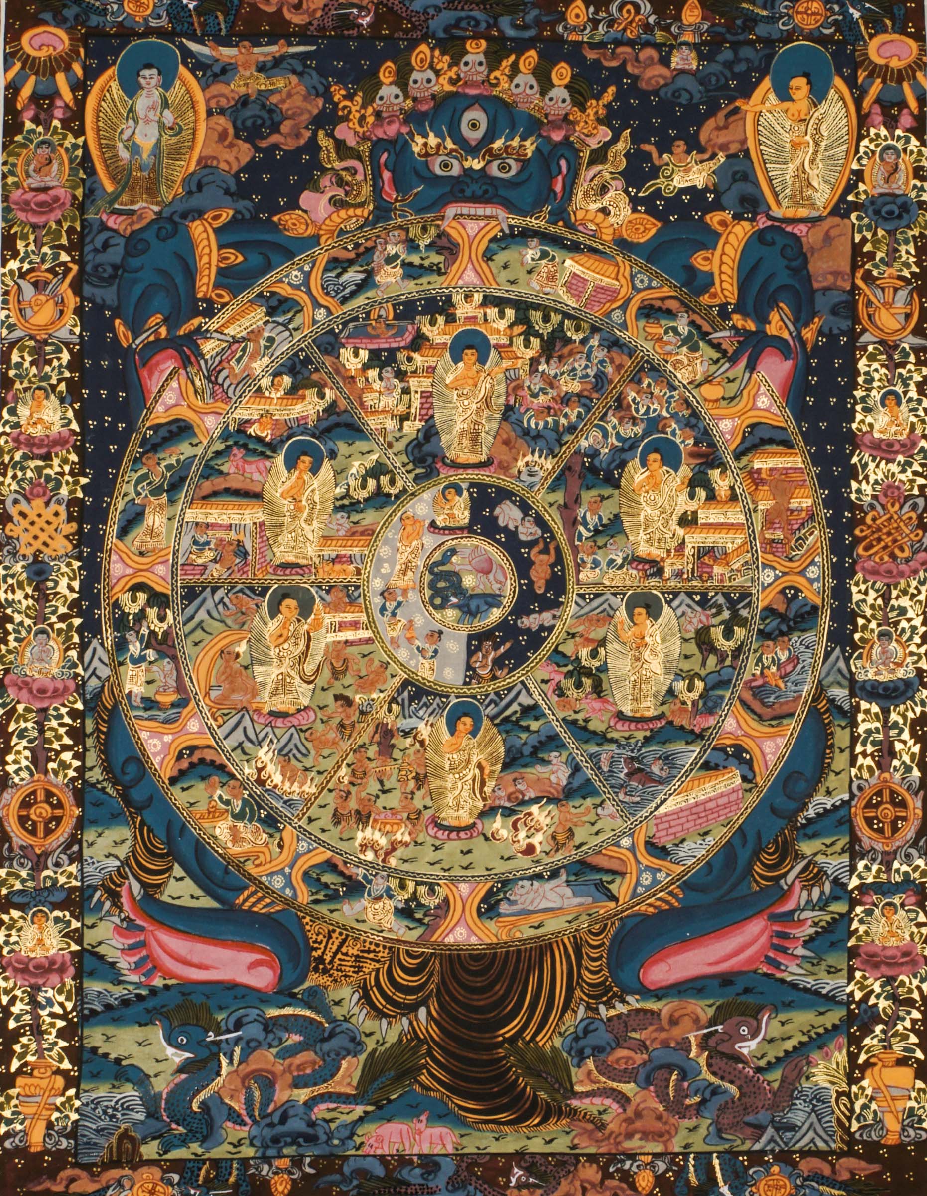 Detailed thangka-style painting showing a large circular wheel divided into multiple sections filled with small human figures, animals, buildings, and landscape scenes, surrounded by concentric decorative rings and held by a large blue multi-eyed figure with extended arms, set against a dark background with clouds, flames, and ornate gold, red, and blue patterns.