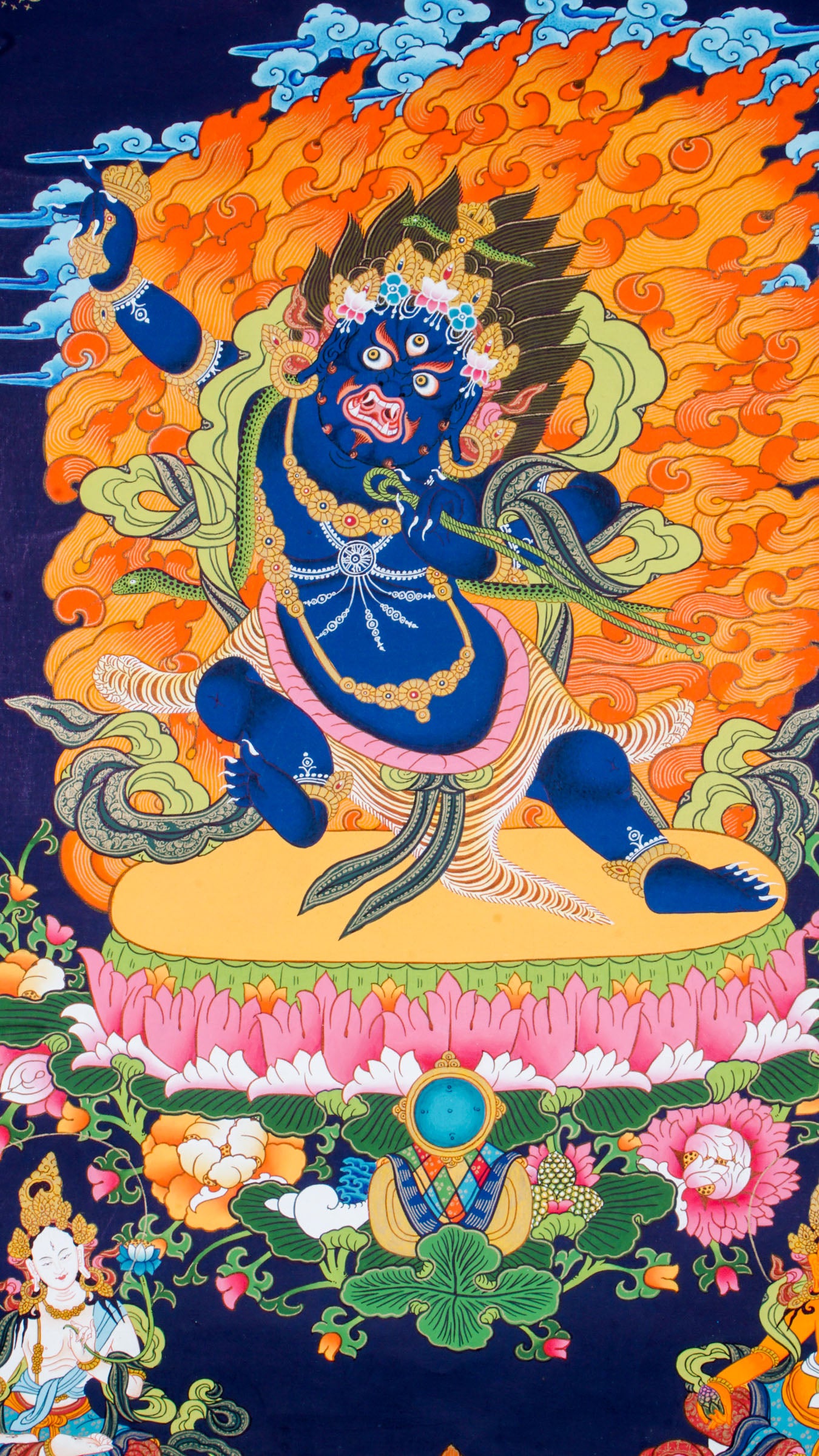 Traditional Tibetan thangka painting depicting wrathful Vajrapani, a blue-skinned deity in a powerful dynamic pose on a lotus throne, surrounded by blazing flames, clouds, and ornate symbolic details against a deep blue background.