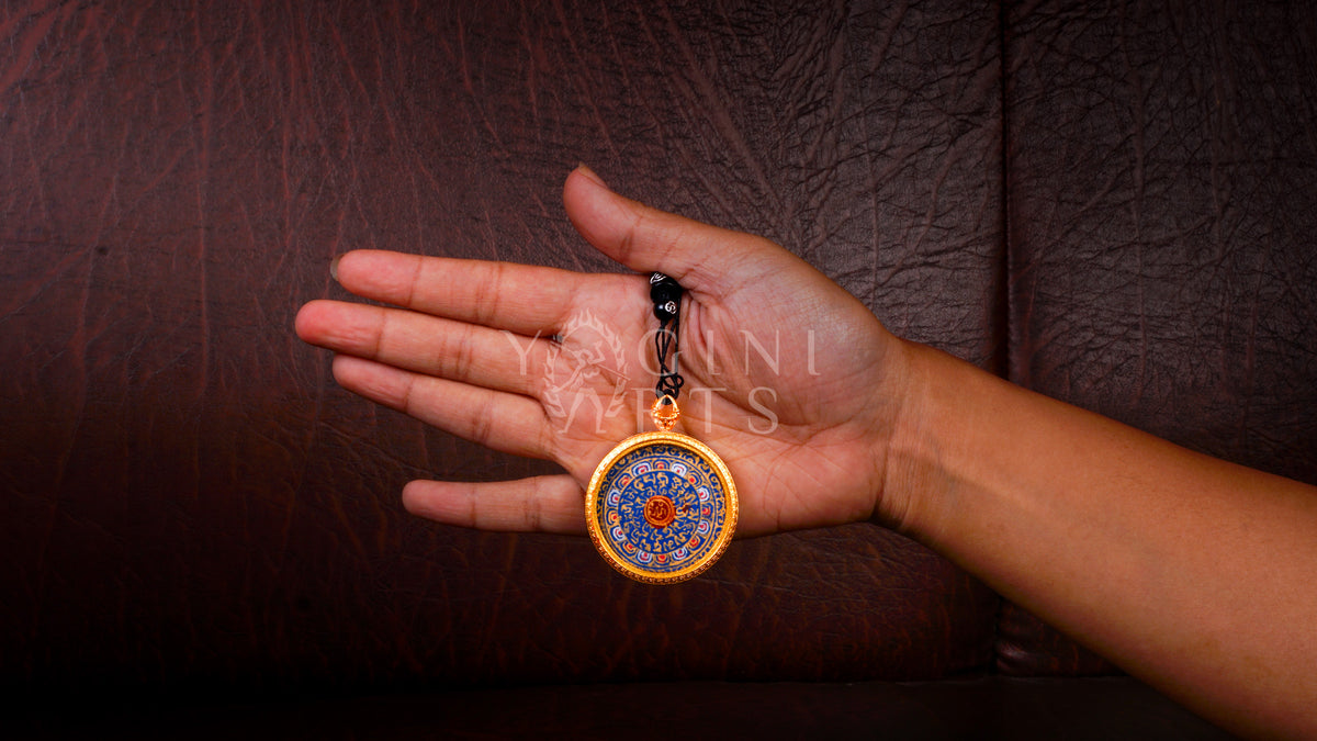 Hand-painted Mantra Mandala Ghau pendant featuring the sacred OM symbol and Tibetan Buddhist mantras in a handcrafted gold-tone frame.
