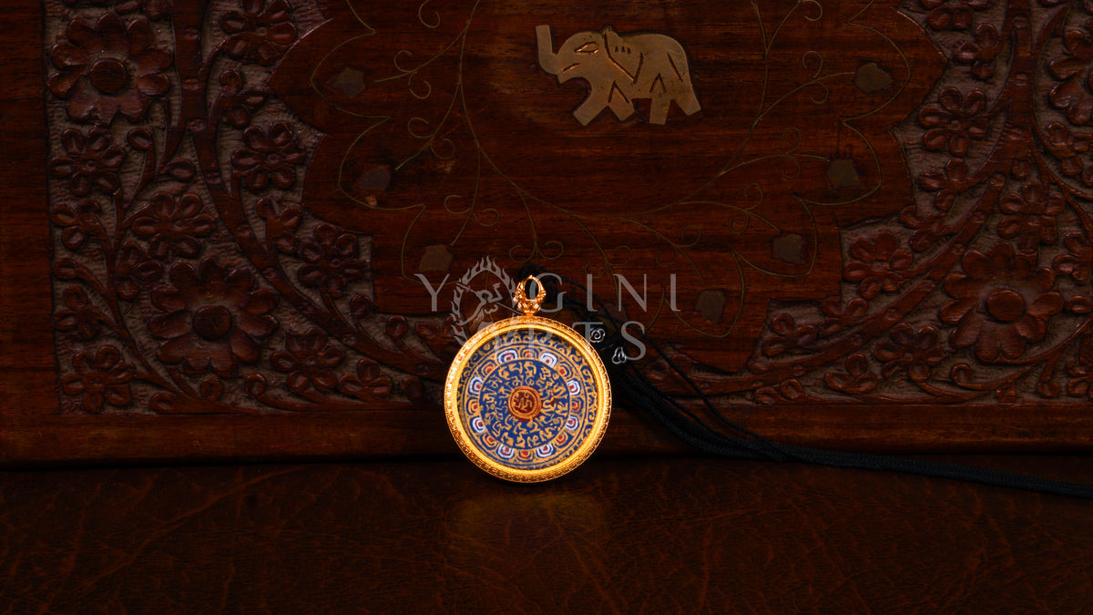 Hand-painted Mantra Mandala Ghau pendant featuring the sacred OM symbol and Tibetan Buddhist mantras in a handcrafted gold-tone frame.