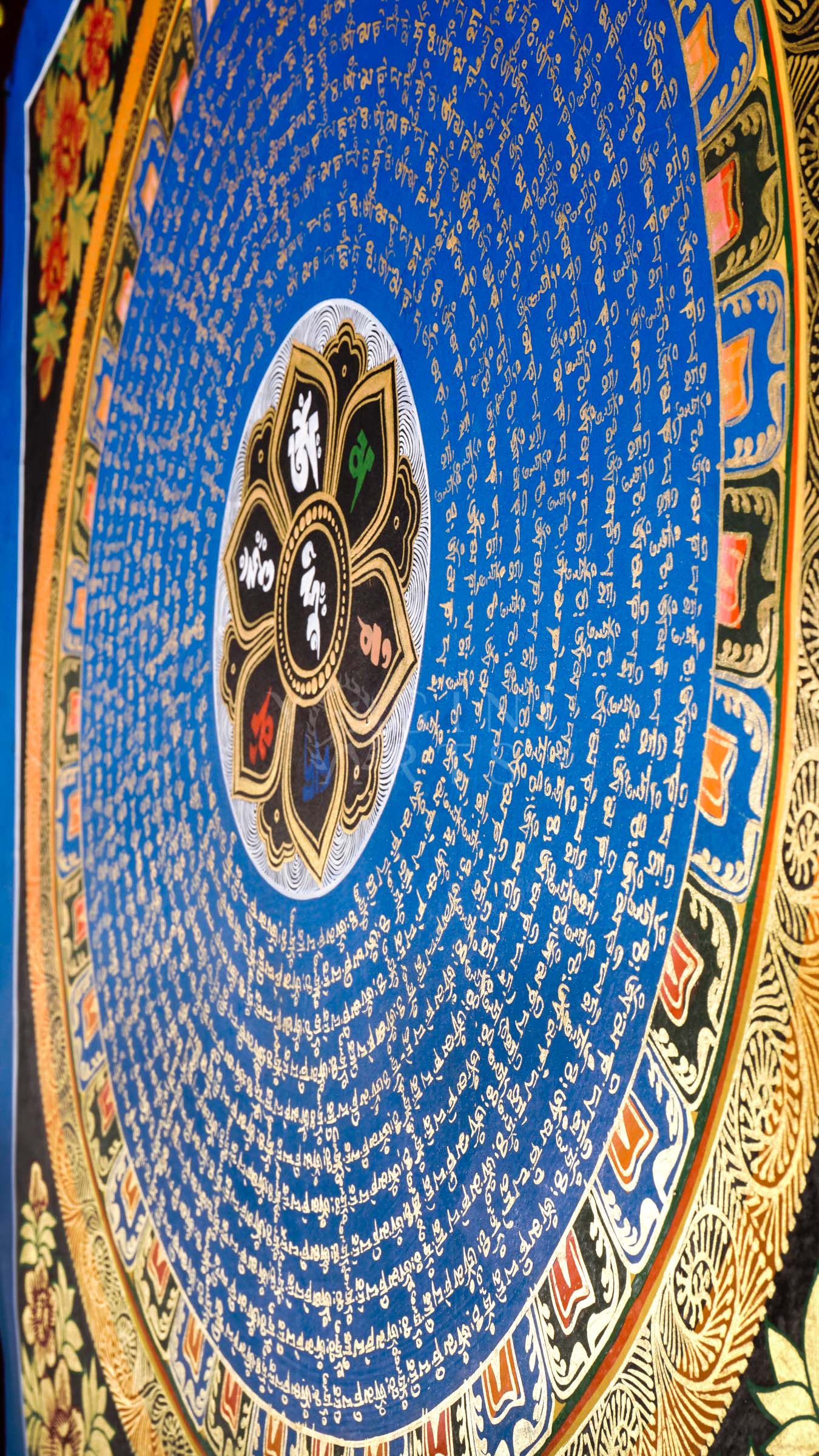 Hand-painted Tibetan Blue Mantra Mandala thangka featuring sacred Tibetan calligraphy arranged in concentric circles around a central lotus emblem with ornate floral borders.