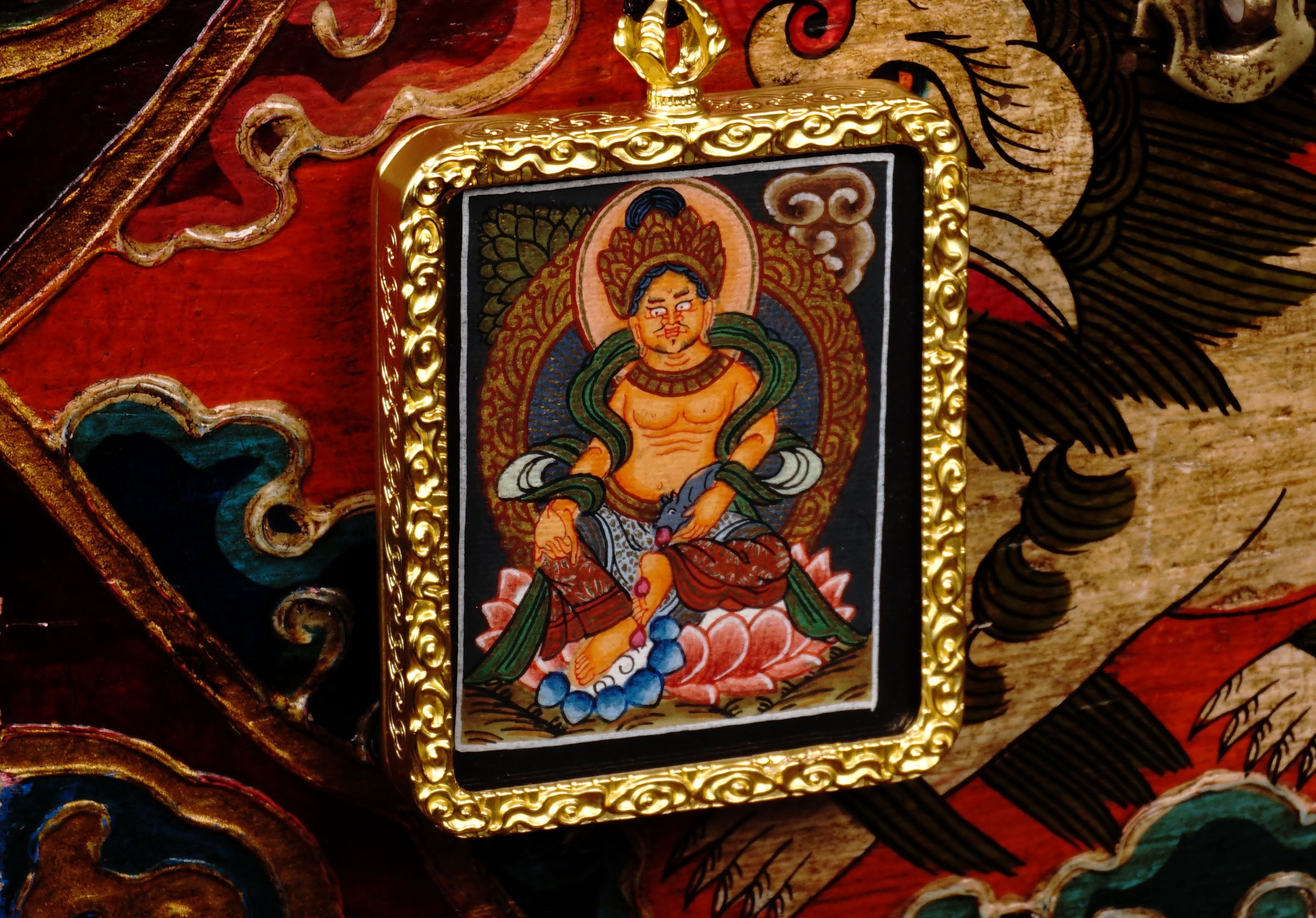 Hand-painted Zambala miniature Thangka pendant in gold-accented copper Ghau locket displayed hanging from black beaded cord.
