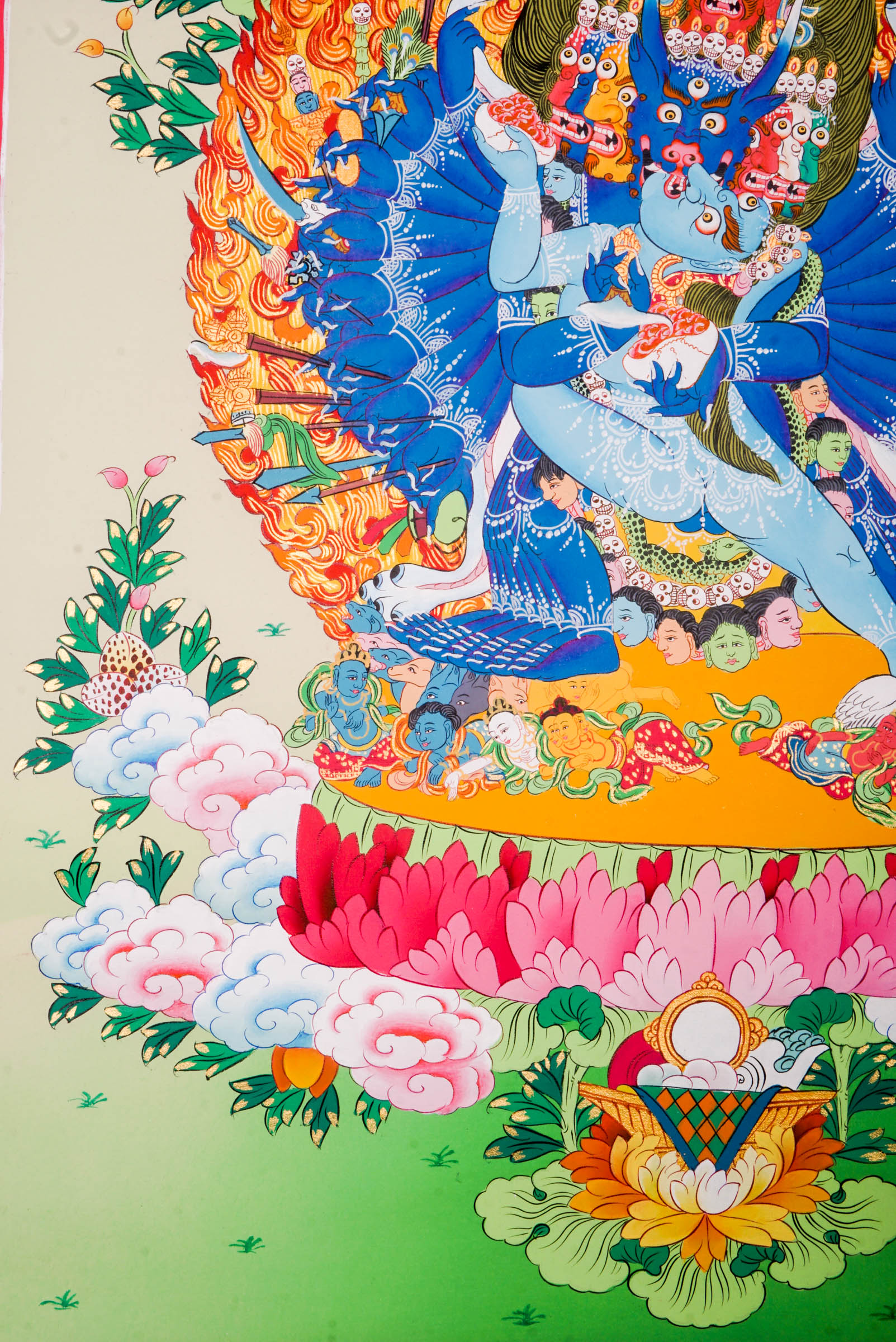 Traditional Tibetan thangka painting depicting Yamantaka Shakti in dynamic embrace, surrounded by flames, clouds, and abundant floral motifs, rendered in vivid colors against a green and turquoise landscape.