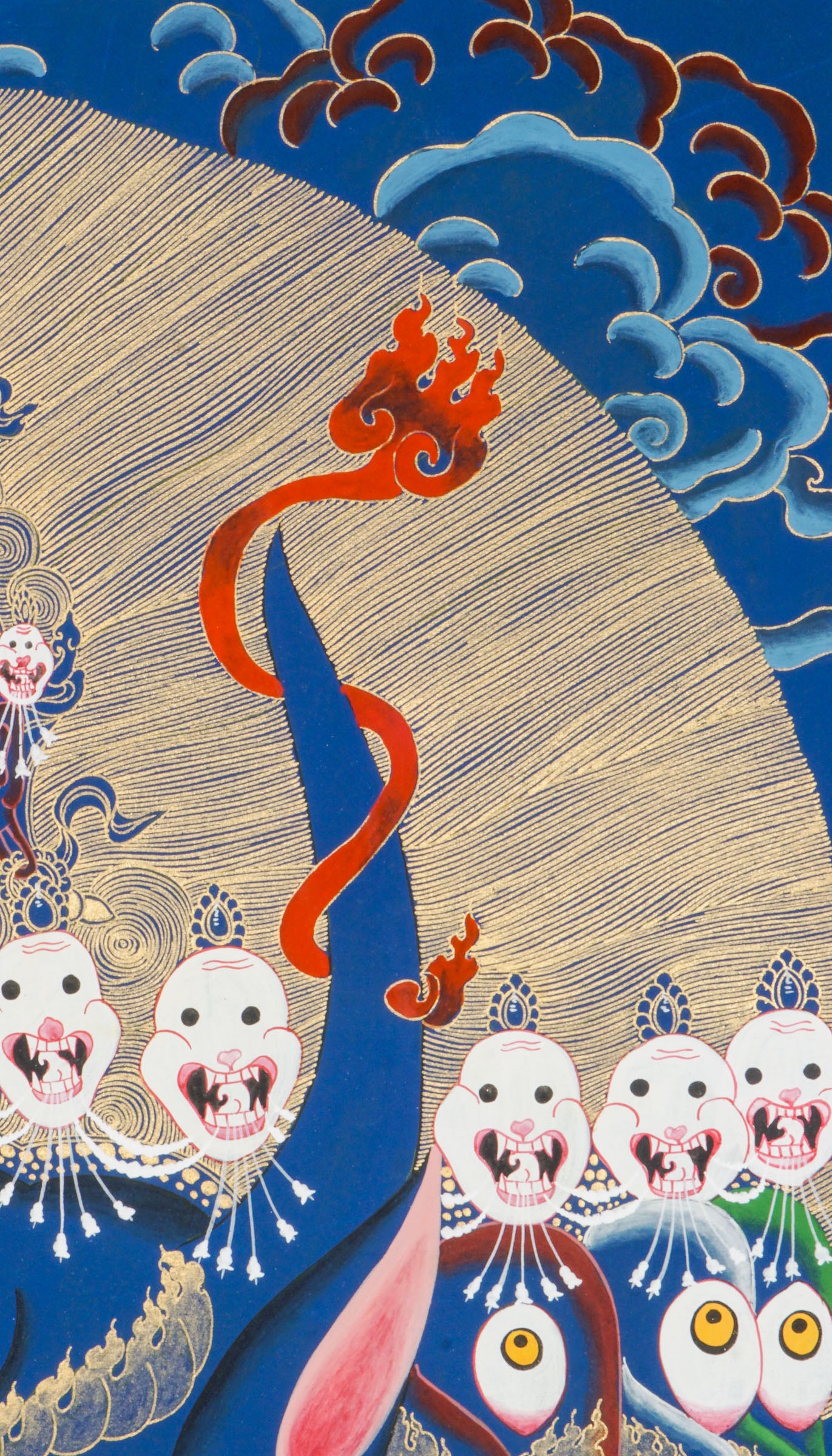 Thangka painting showing a large blue multi-faced figure with numerous eyes and open mouths, crowned by smaller faces and skull motifs, set against a gold halo and stylized cloud background.