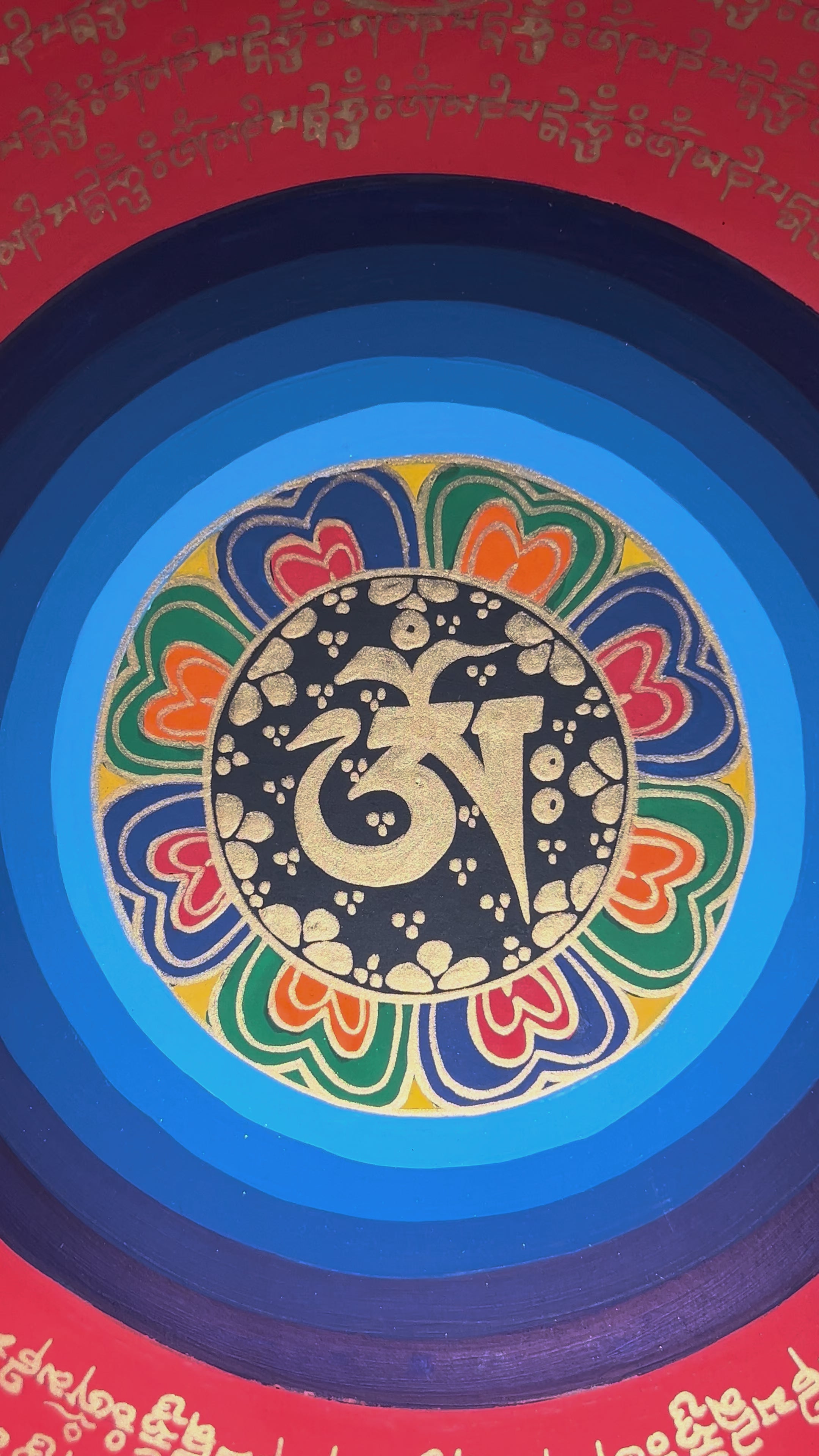 Tibetan mantra mandala thangka with black background, multicolor central rings, gold script circles, and floral corner designs.