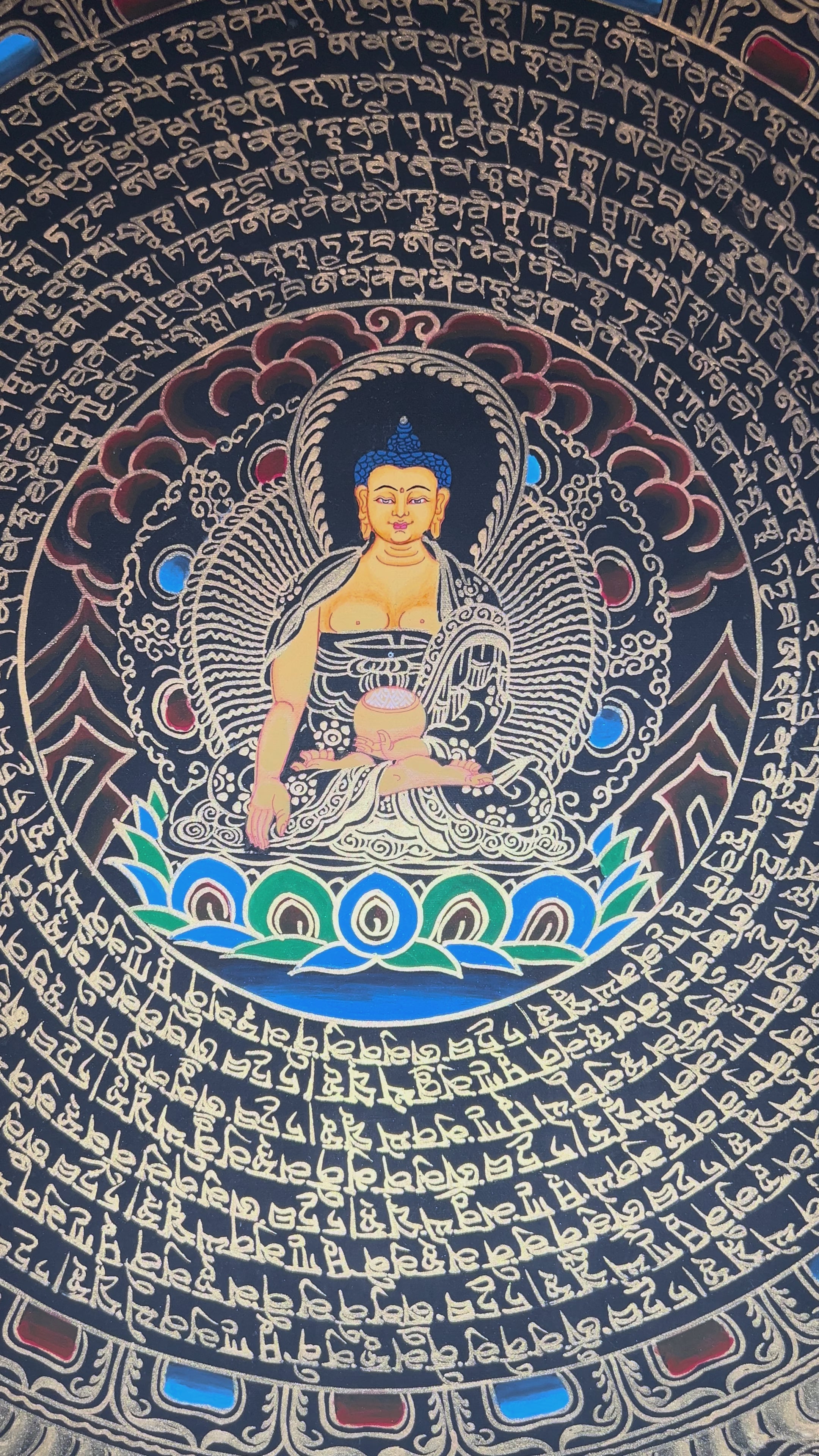 Shakyamuni Buddha mandala thangka featuring a central Buddha figure surrounded by circular Tibetan script and intricate gold detailing on a black background.