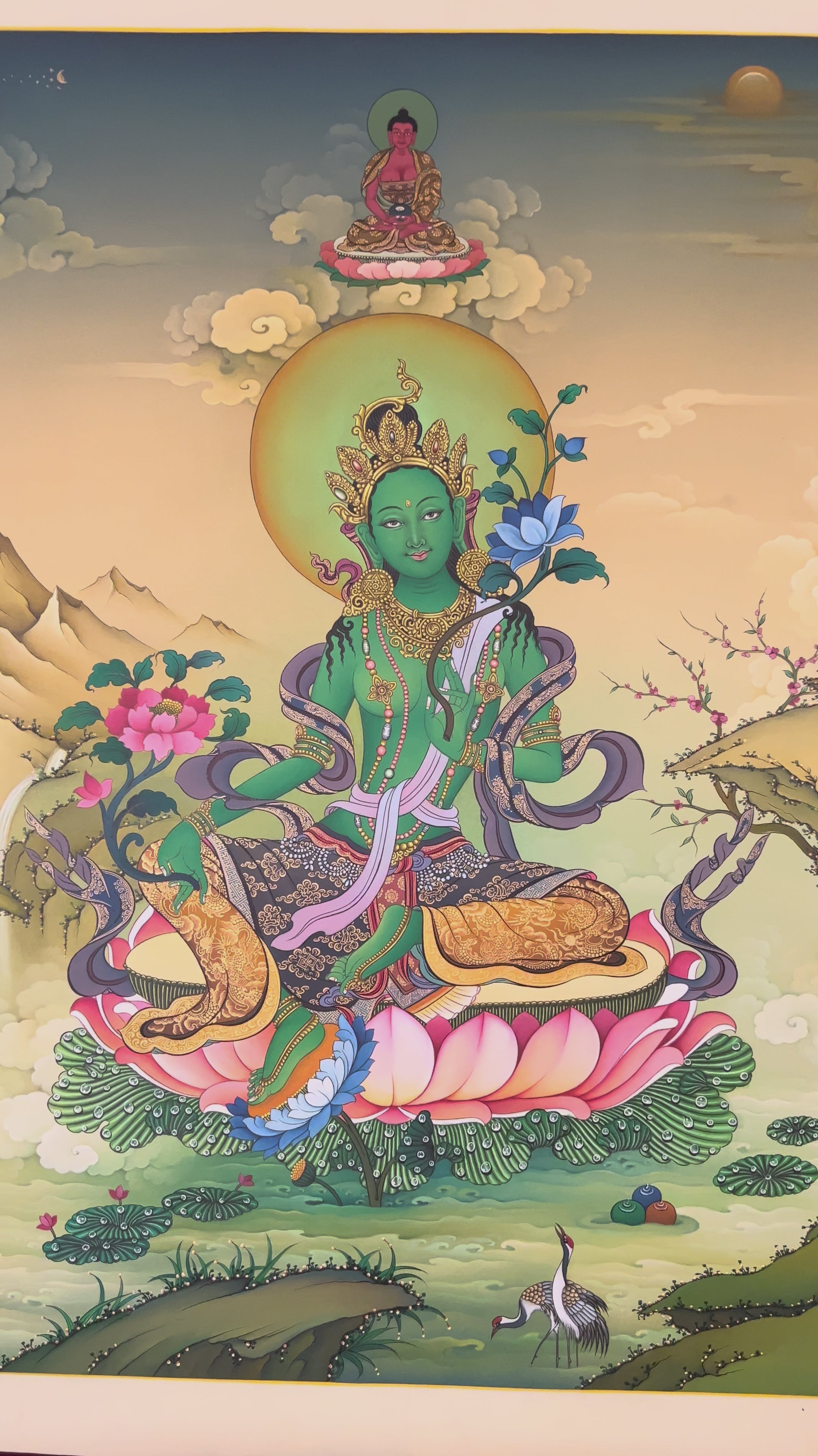 Hand-painted Green Tara thangka showing Tibetan Buddhist goddess seated on lotus throne holding blue utpala lotus, with Amitabha above and Himalayan landscape background.