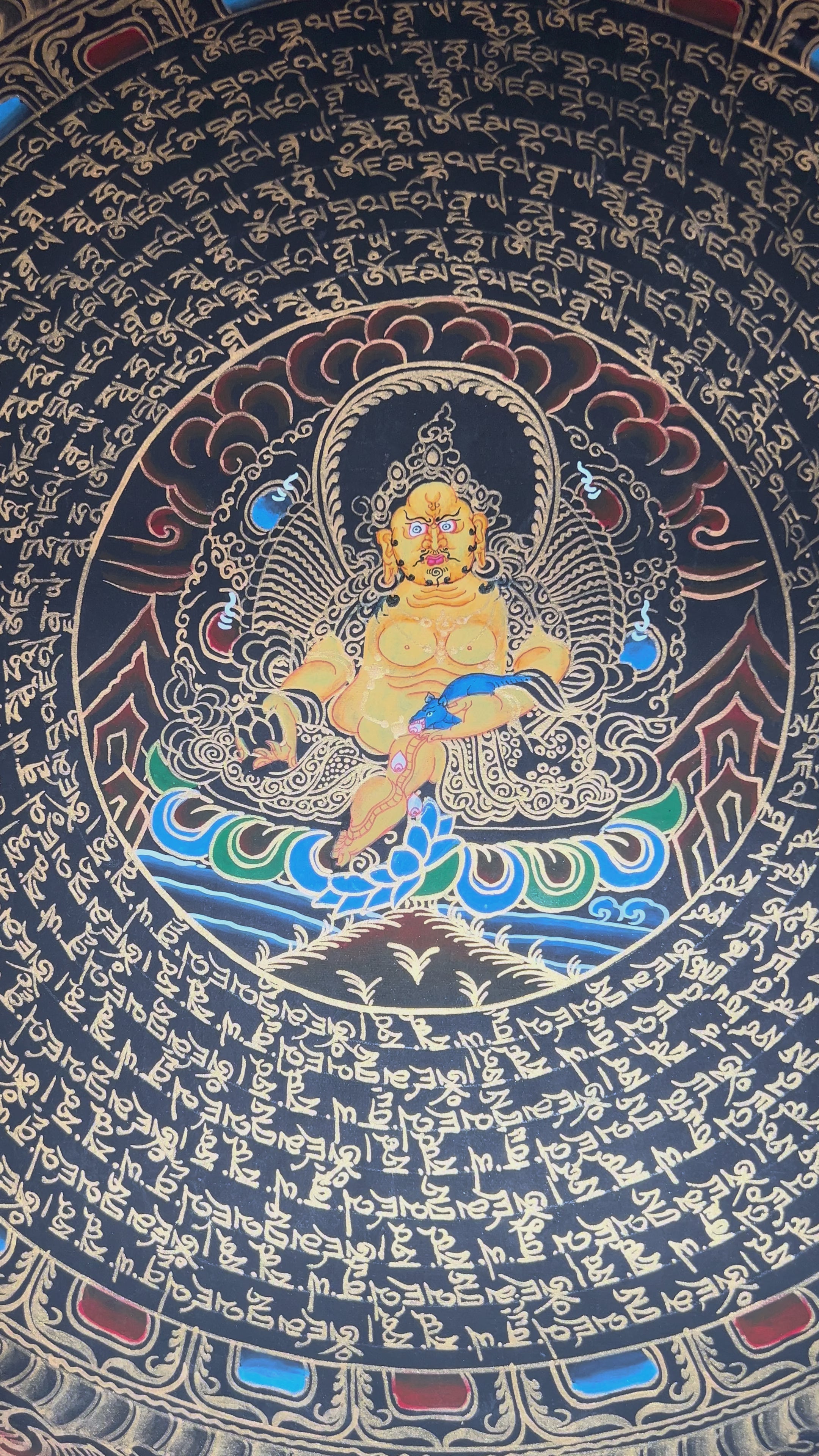 Zambhala mandala thangka featuring a central wealth deity surrounded by circular Tibetan script and intricate gold detailing on black background.