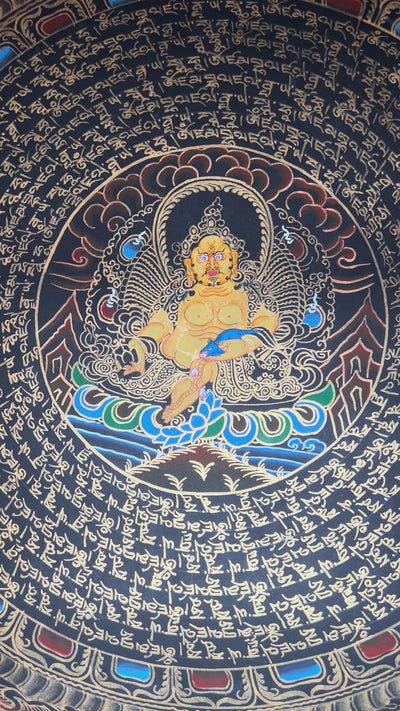 Zambhala mandala thangka featuring a central wealth deity surrounded by circular Tibetan script and intricate gold detailing on black background.