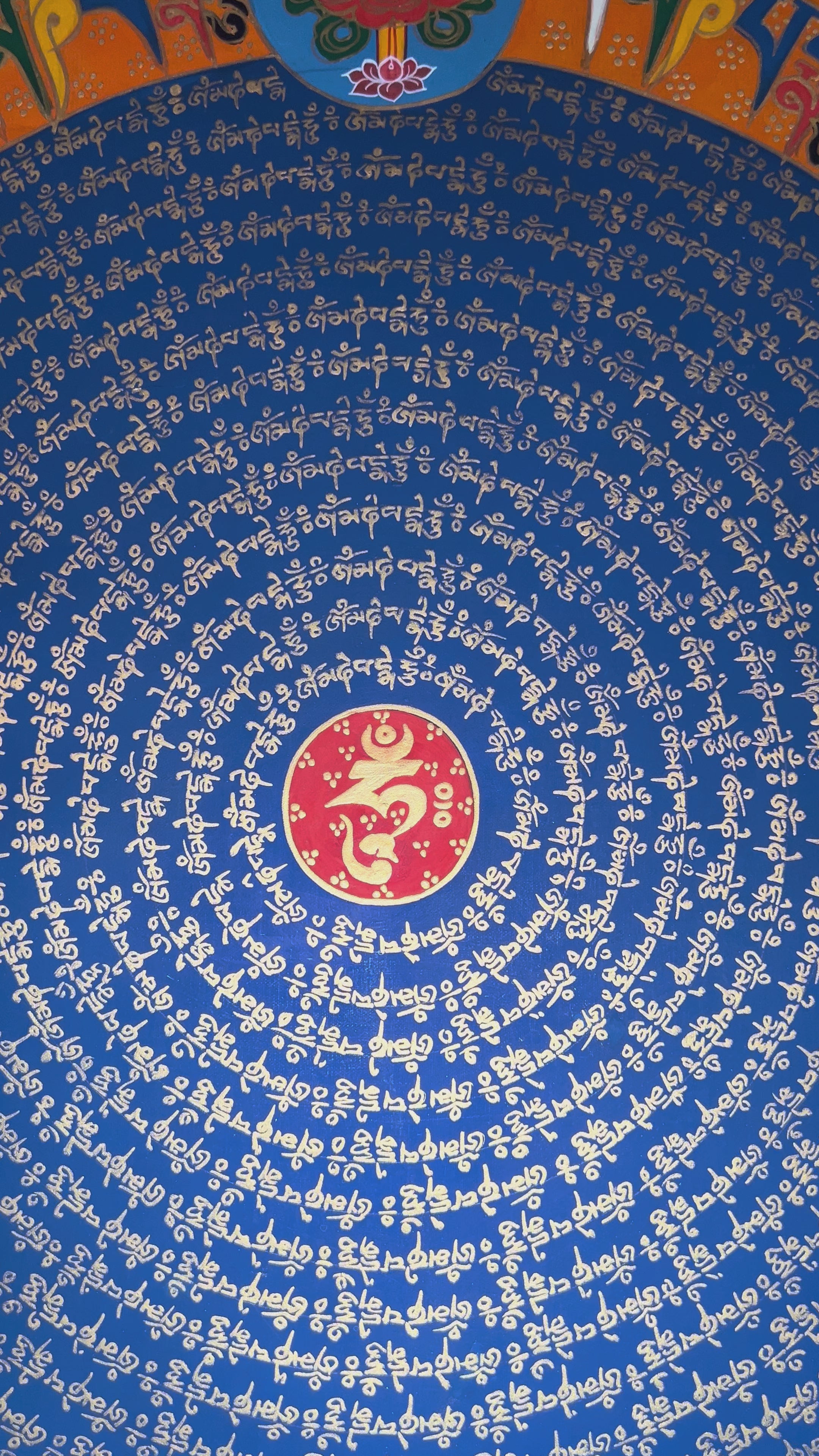 Tibetan mantra mandala thangka with blue center, gold script rings, orange band featuring eight auspicious symbols, and ornate golden border.