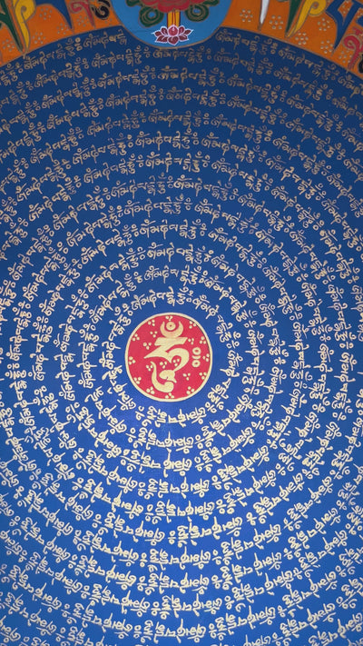 Tibetan mantra mandala thangka with blue center, gold script rings, orange band featuring eight auspicious symbols, and ornate golden border.