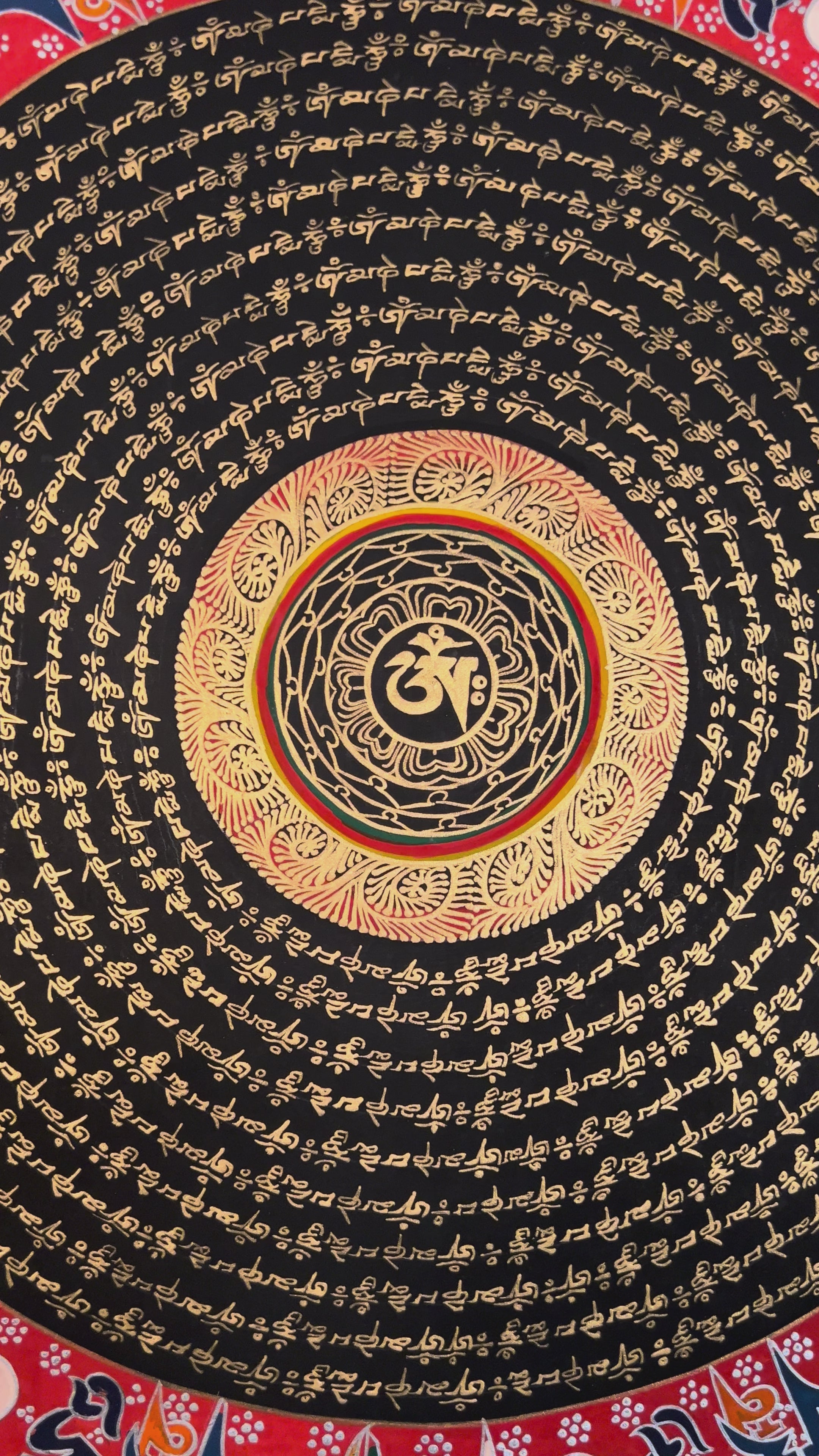 Tibetan mantra mandala thangka with black background, gold script rings, bold red outer mantra band, and floral corner decorations.