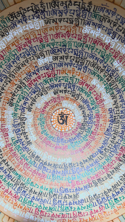 Small Tibetan mantra mandala thangka with multicolor script spiraling around Om symbol on a gold background with floral corner designs.