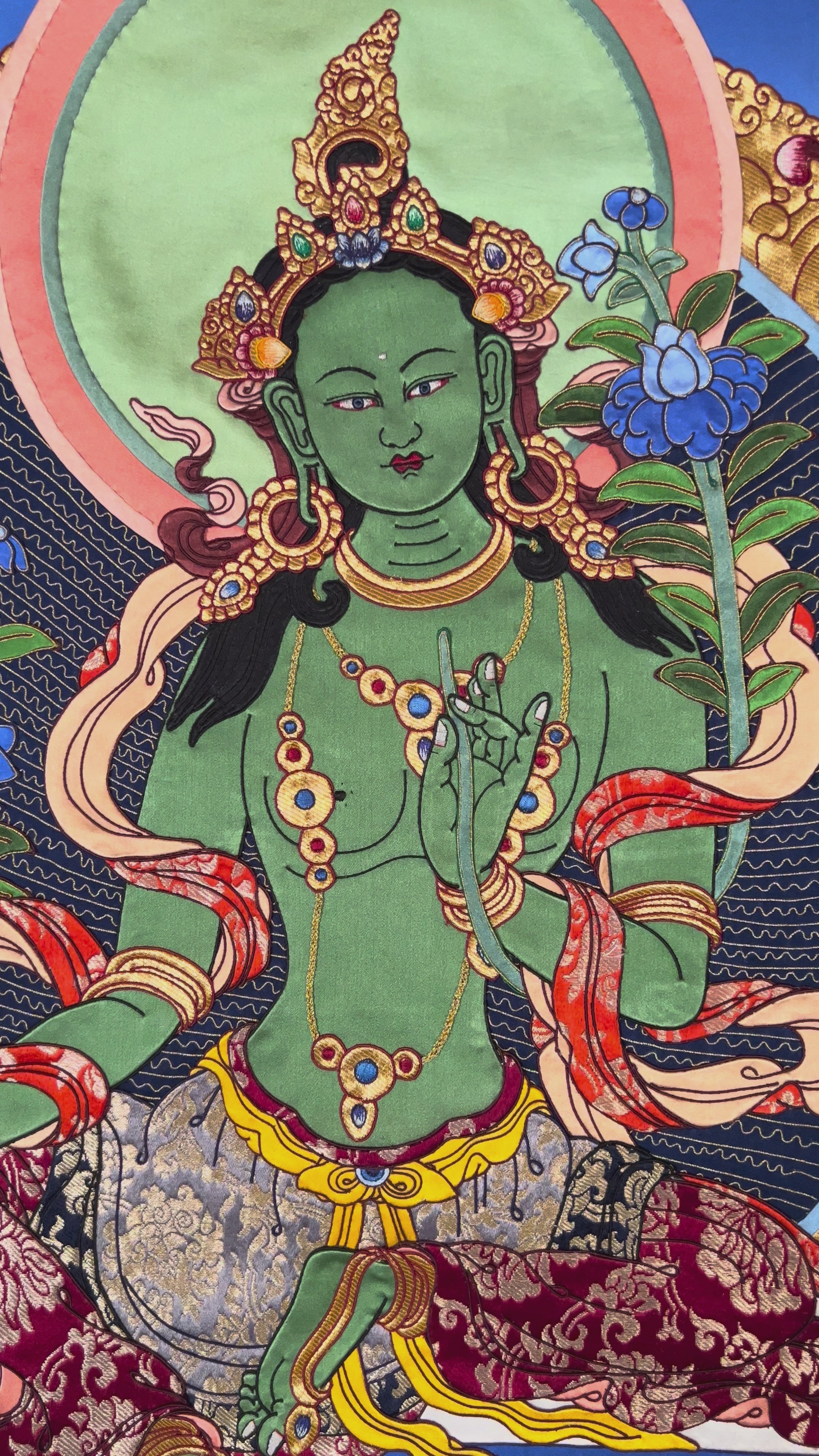 Green Tara cloth thangka printed on fabric showing Tibetan Buddhist goddess seated on lotus holding blue utpala lotus with vibrant halo background.
