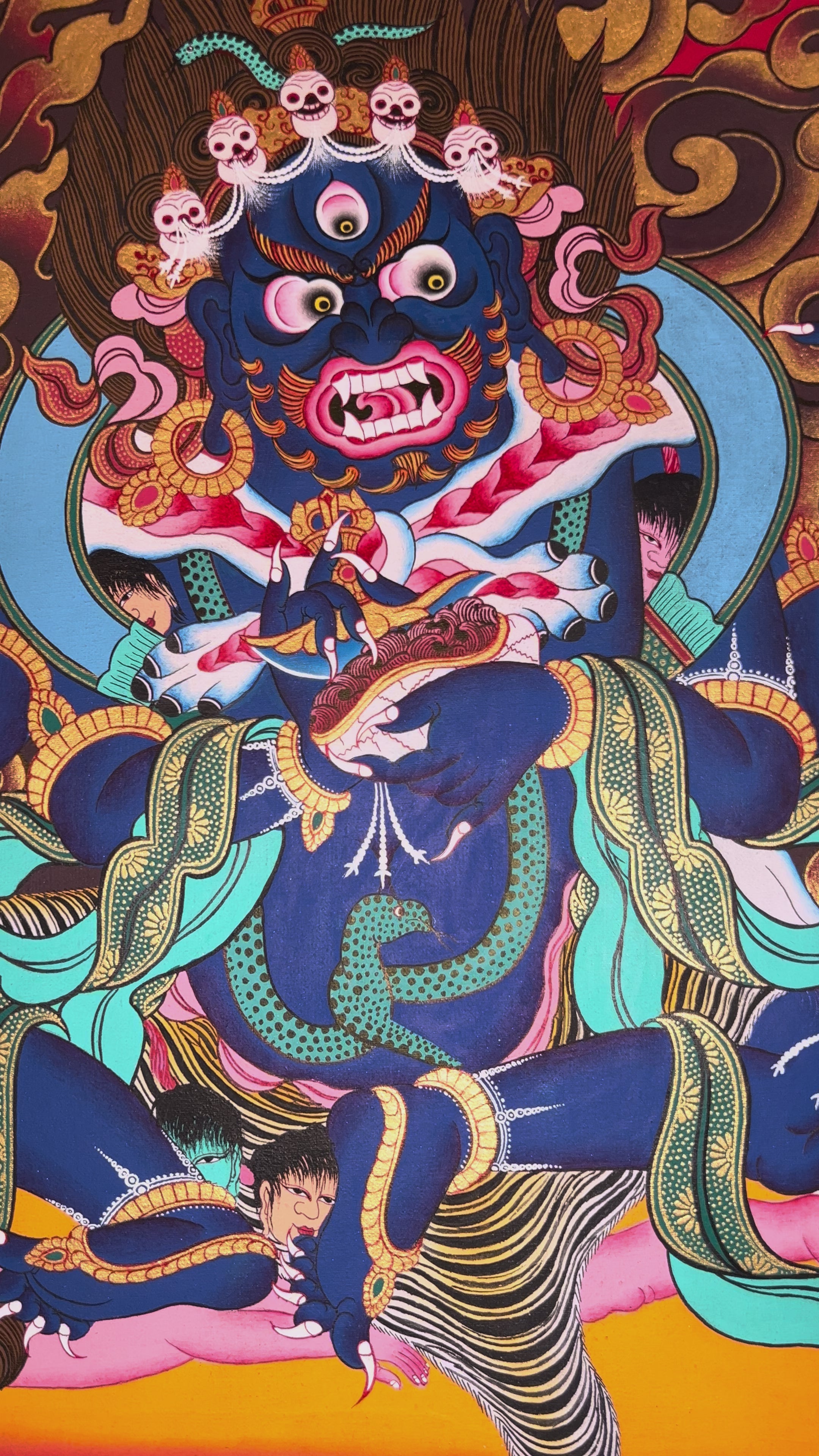 Mahakala thangka showing a fierce blue wrathful deity with multiple arms, surrounded by flames and standing on subdued figures in traditional Tibetan style.