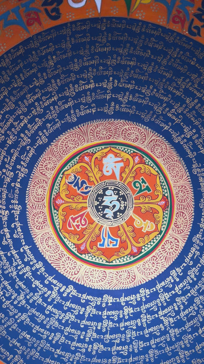 Tibetan mantra mandala thangka with blue background, gold script rings, colorful outer mantra band, and floral corner decorations.